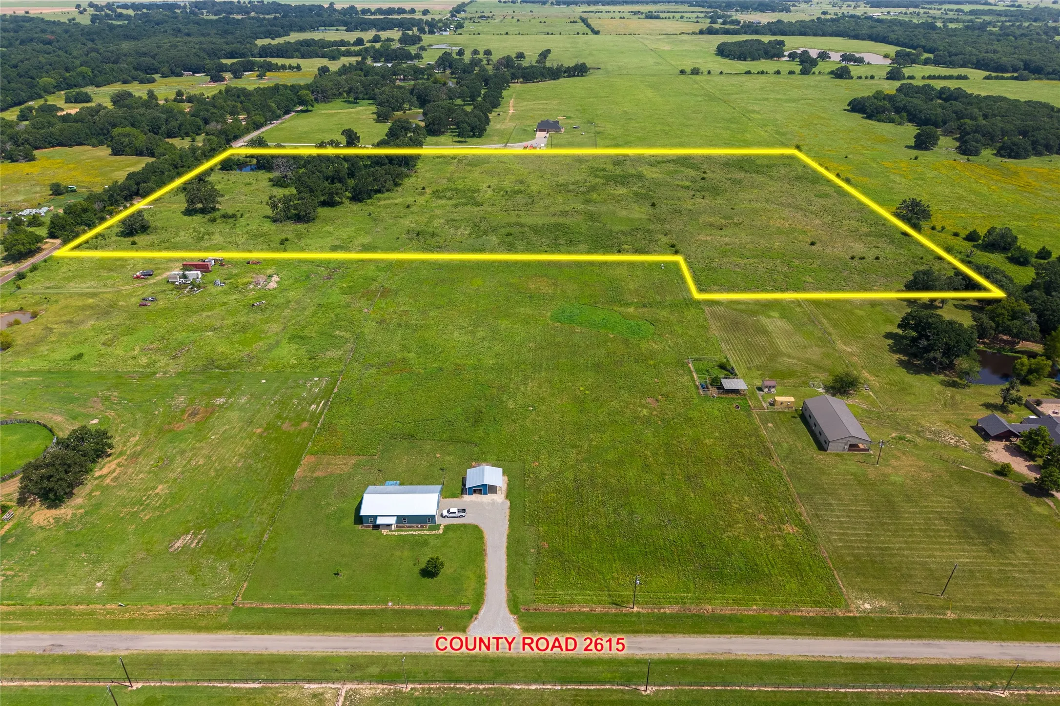 Aerial shot of 27+ acres with mature trees, pond, and open pasture looking S