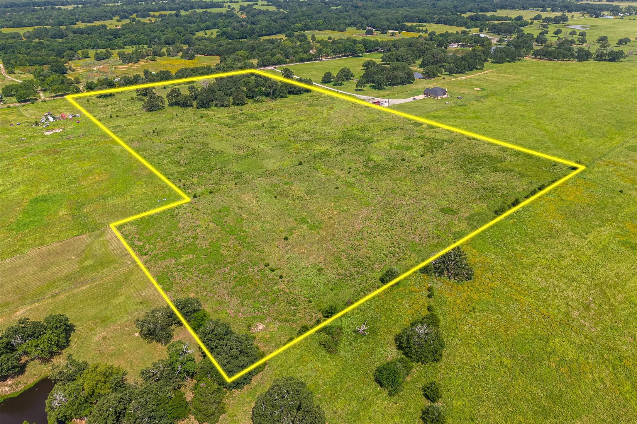 Aerial shot of 27+ acres with mature trees, pond, and open pasture looking SE