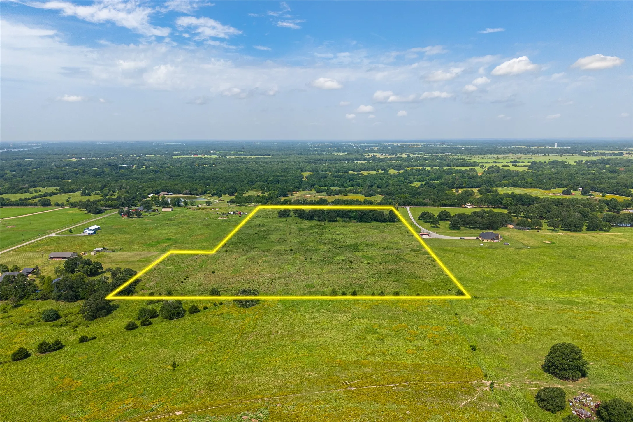 Aerial shot of 27+ acres with mature trees, pond, and open pasture looking E
