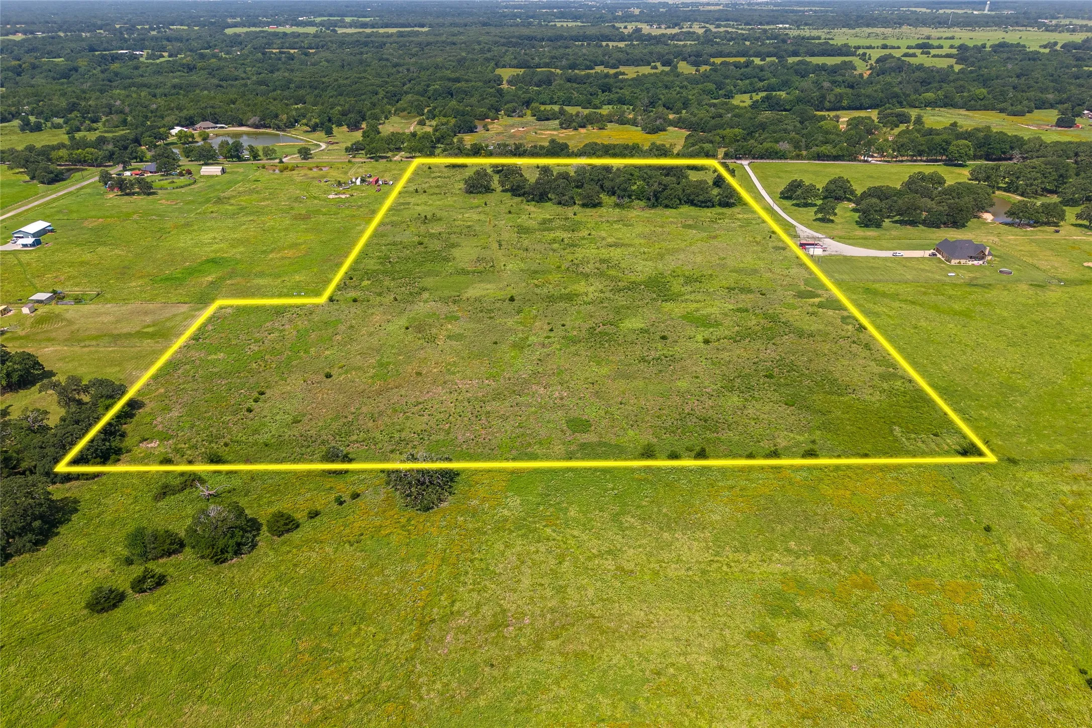 Aerial shot of 27+ acres with mature trees, pond, and open pasture looking E