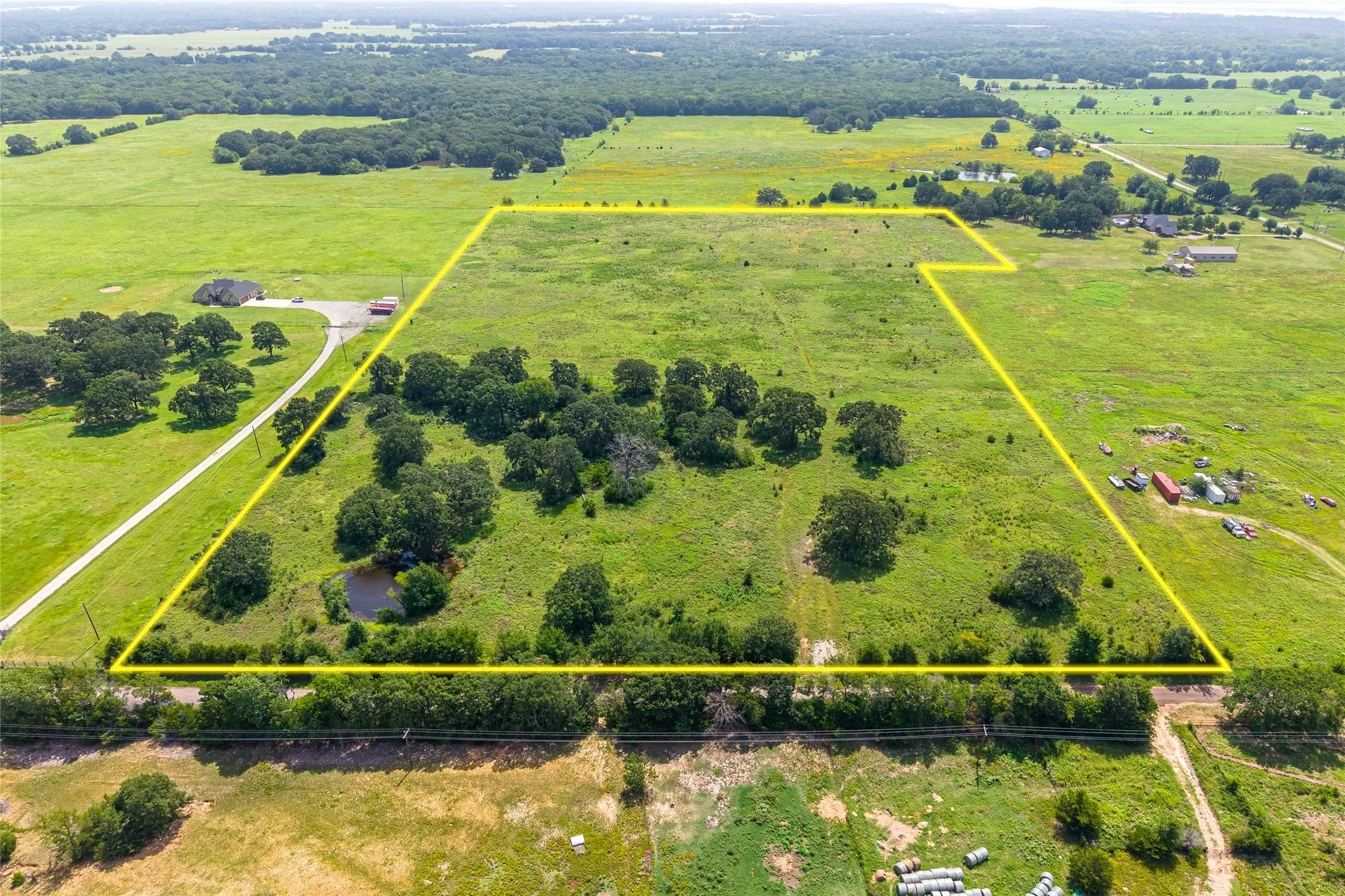 Aerial shot of 27+ acres with mature trees, pond, and open pasture looking W