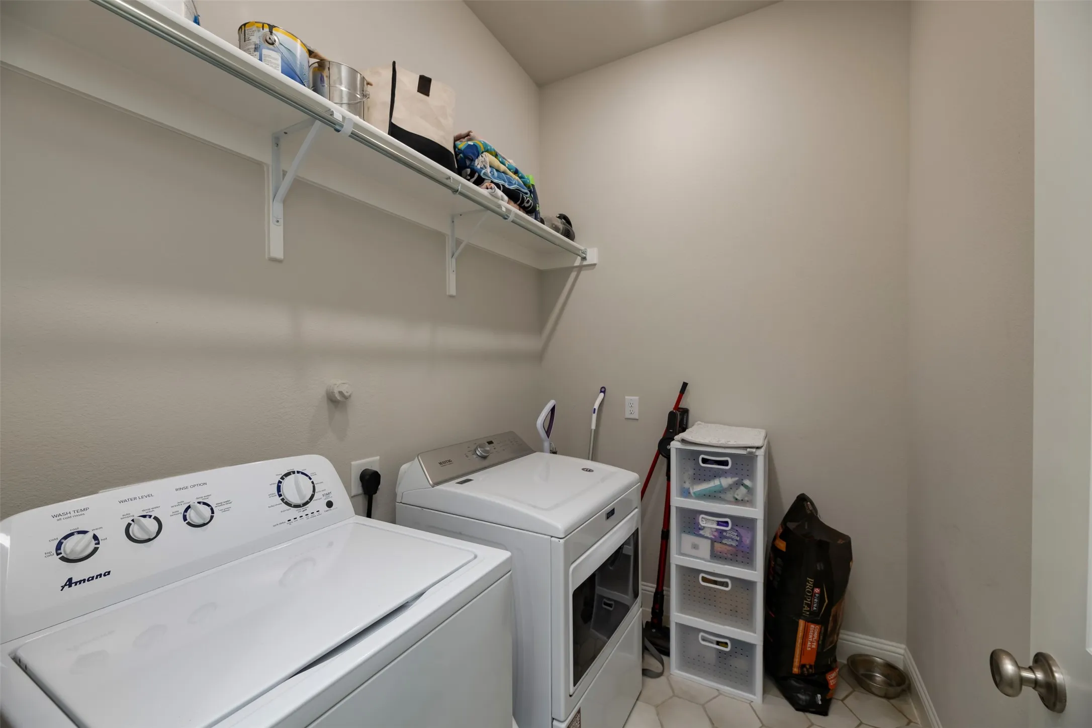 Dedicated laundry area featuring a full-size washer and dryer, upper storage shelving, and hexagonal floor tiling