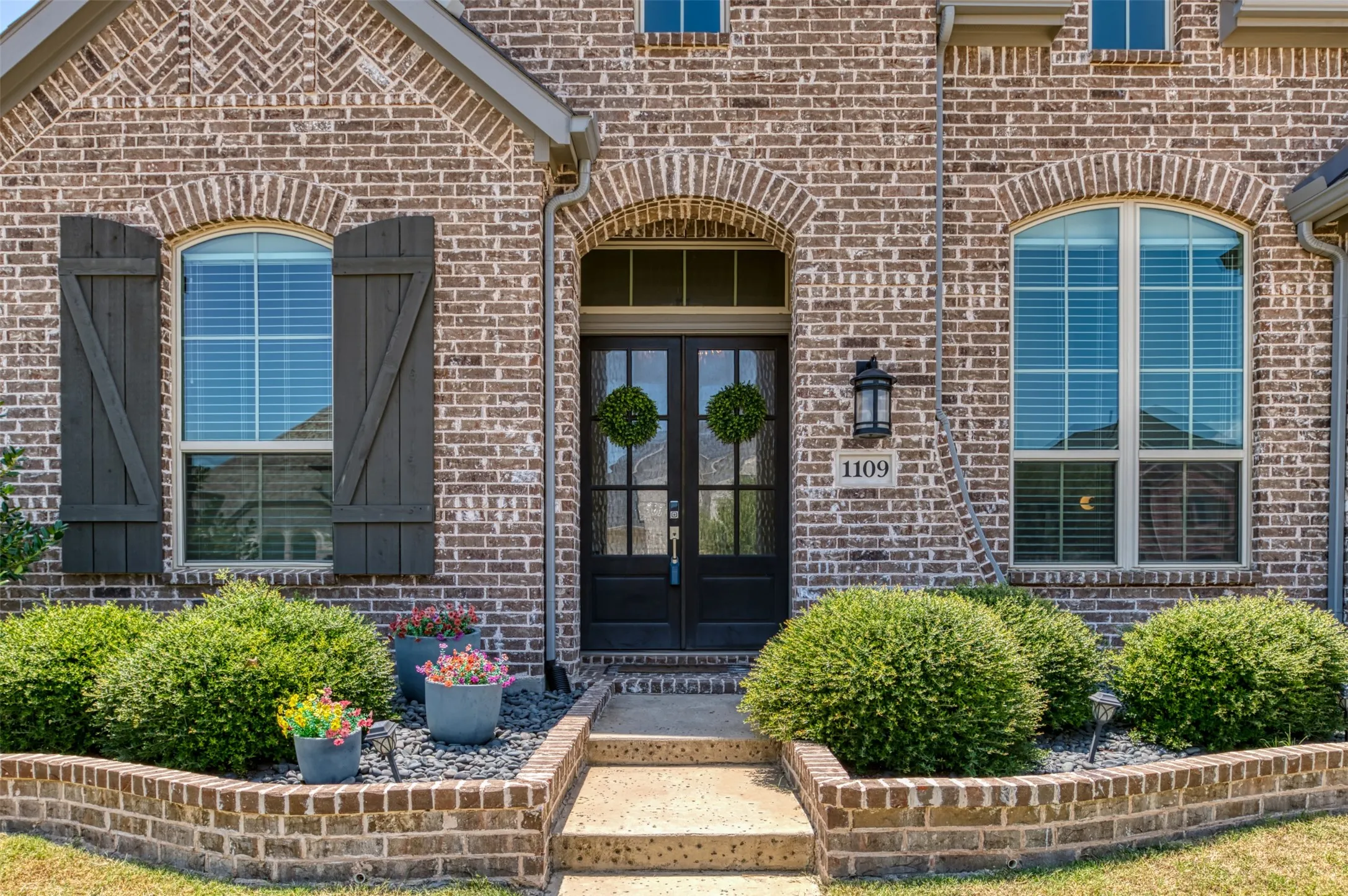 Brick exterior featuring arched window headers, a dual-pane arched entry door, and dark wood shutters