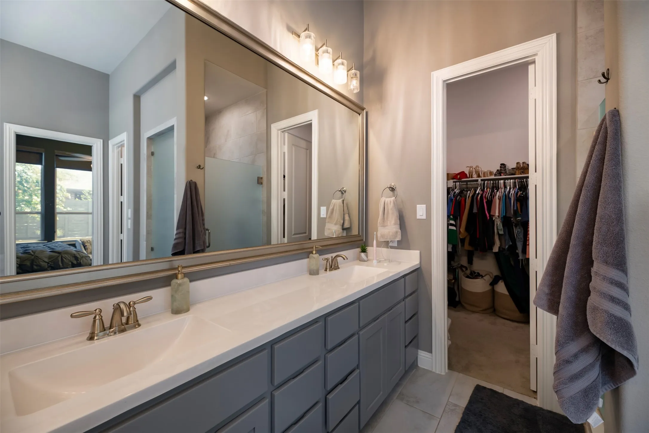 Bathroom vanity featuring dual sinks, a large framed mirror, gray cabinetry, and brass-finish fixtures