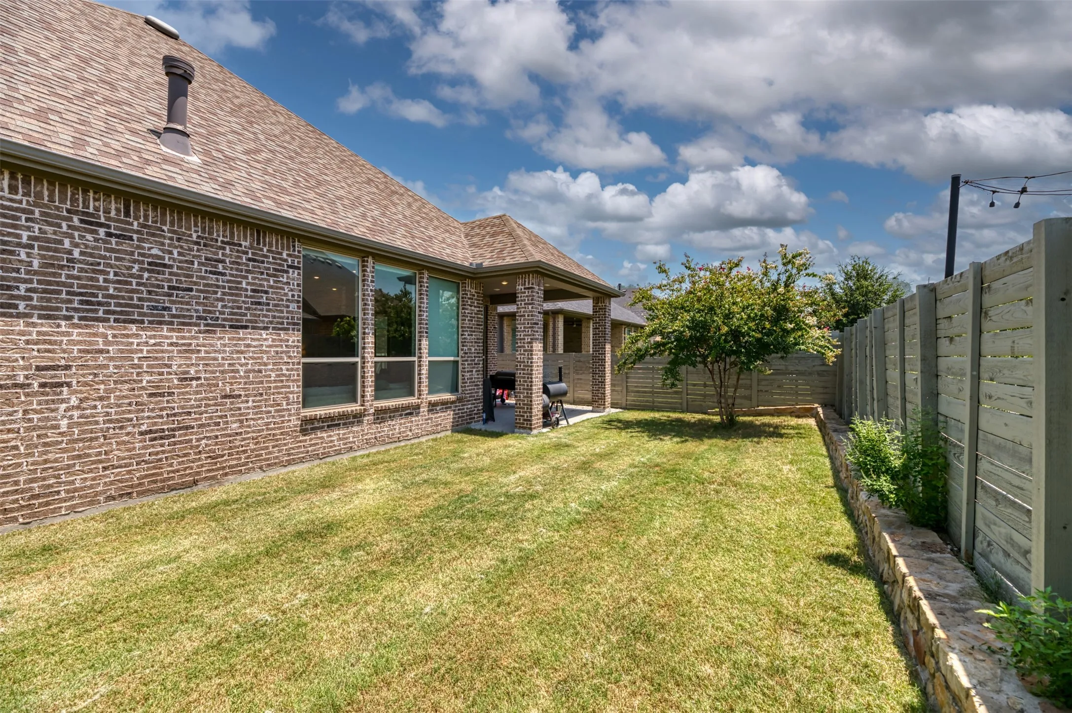 Expansive backyard with a manicured lawn, a mature tree, and a stone retaining wall