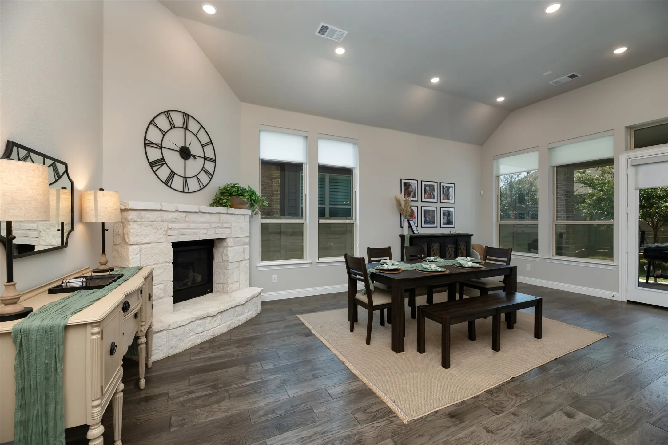 Vaulted ceiling room featuring a stone-clad fireplace, wood-finish flooring, recessed lighting, and multiple windows