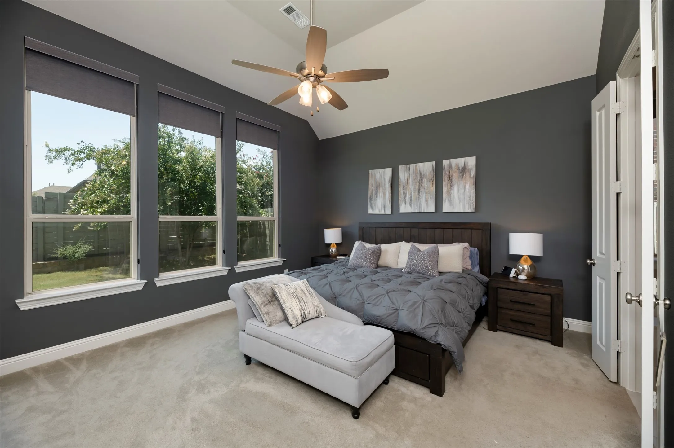 Vaulted ceiling room featuring three large windows, a ceiling fan with integrated lighting, soft carpet flooring, and bi-fold doors