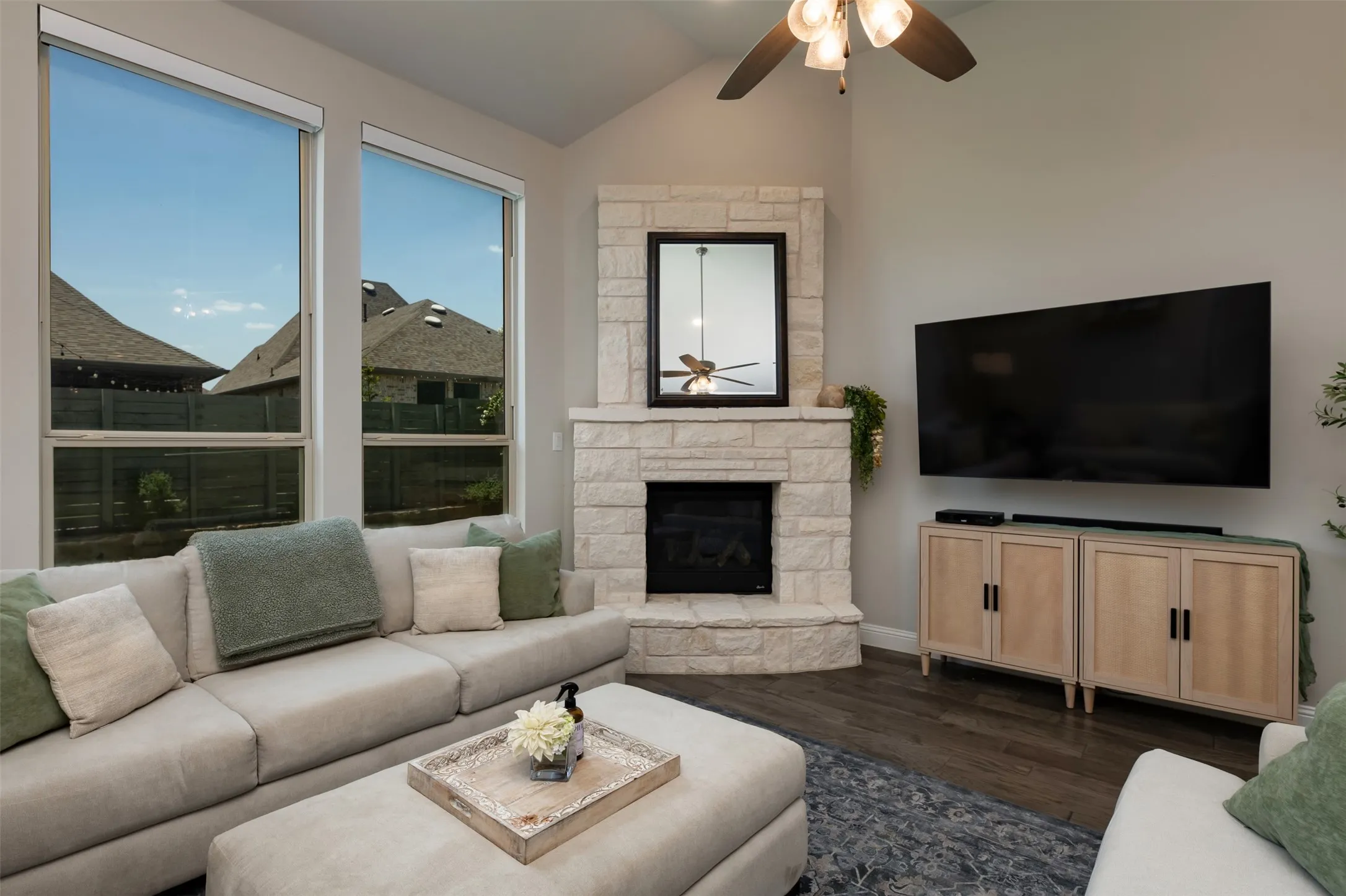 Living area featuring a stone-clad fireplace, dark wood-finish flooring, and a vaulted ceiling with a ceiling fan