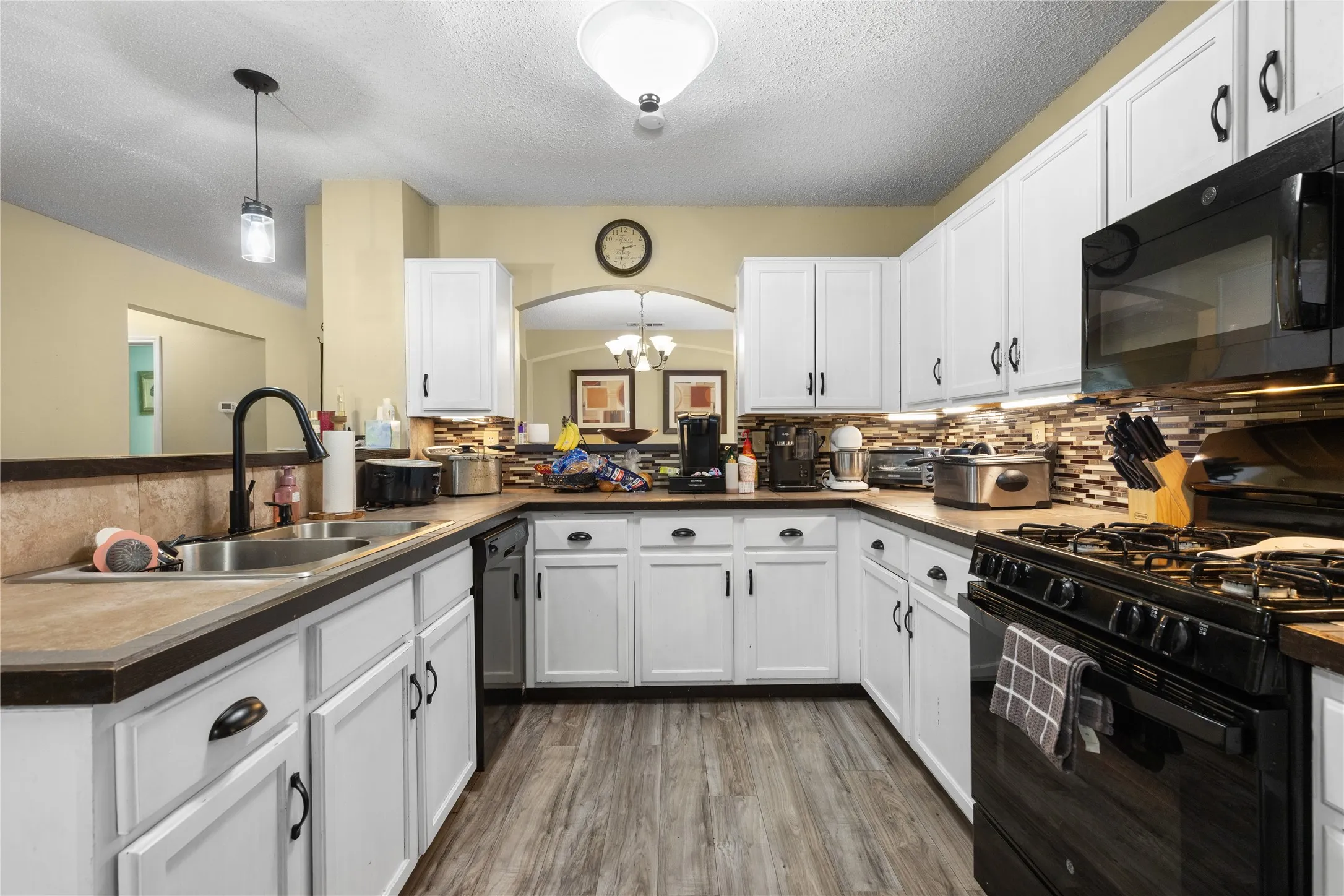 U-shaped kitchen featuring white cabinetry, dark countertops, a tile backsplash, and a black appliance suite
