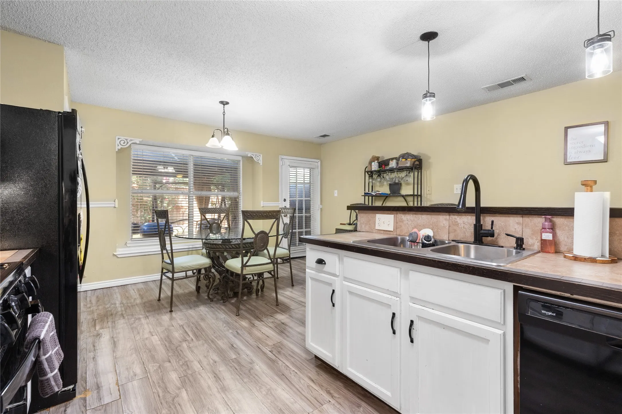 Kitchen featuring wood-finish flooring, white cabinetry, a double basin sink with a black gooseneck faucet, and a black dishwasher