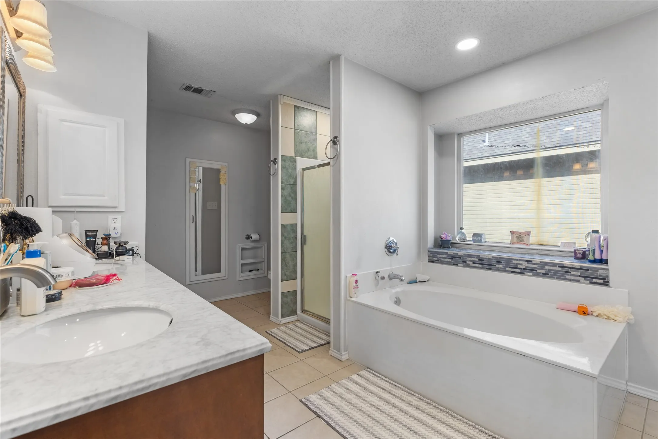 Bathroom featuring a built-in soaking tub, a separate tiled shower with glass enclosure, a vanity with a white countertop and integrated sink, and light tile flooring