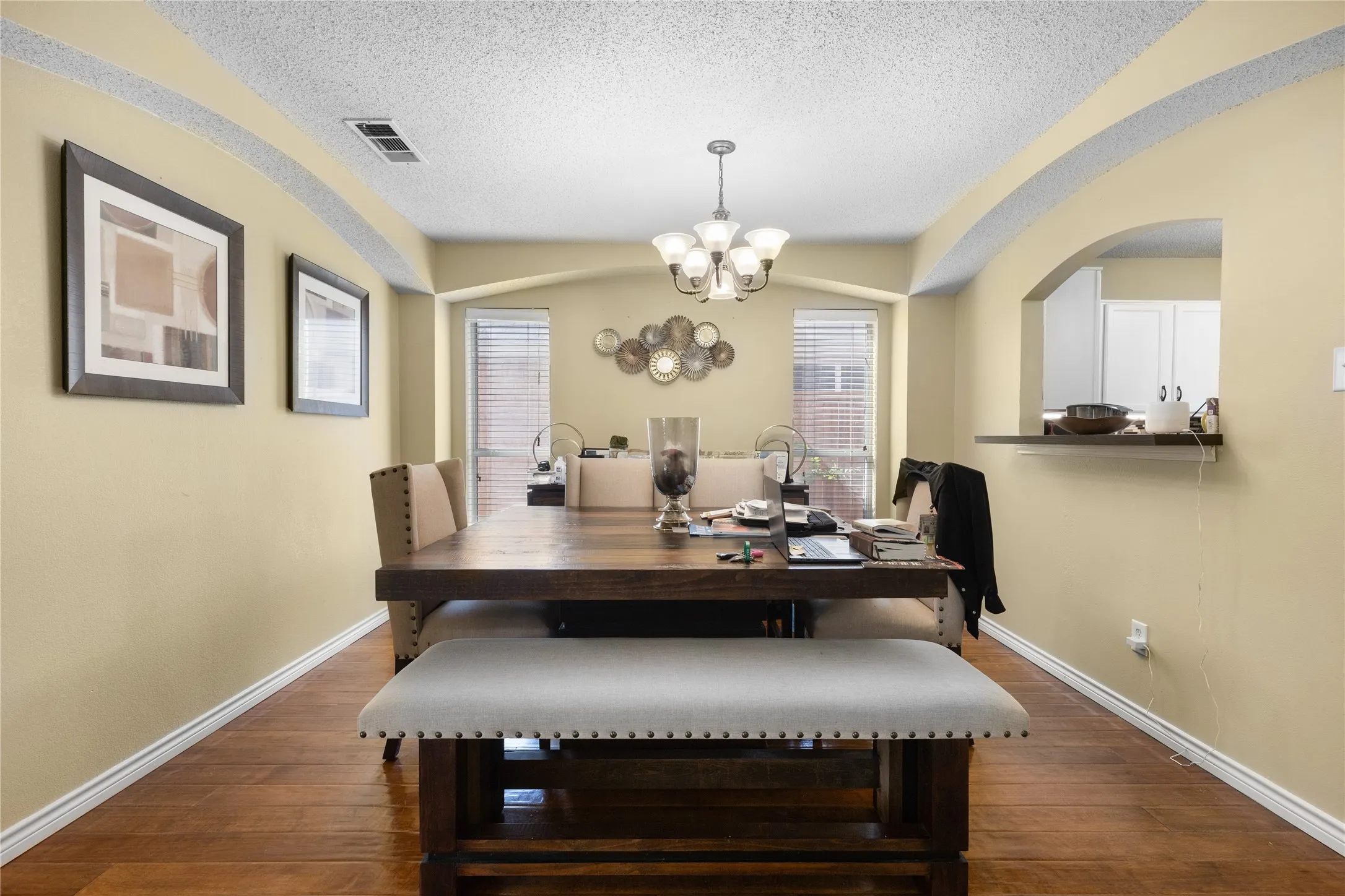 Dining area featuring wood-finish flooring, a contemporary chandelier, two large windows with blinds, and decorative archways