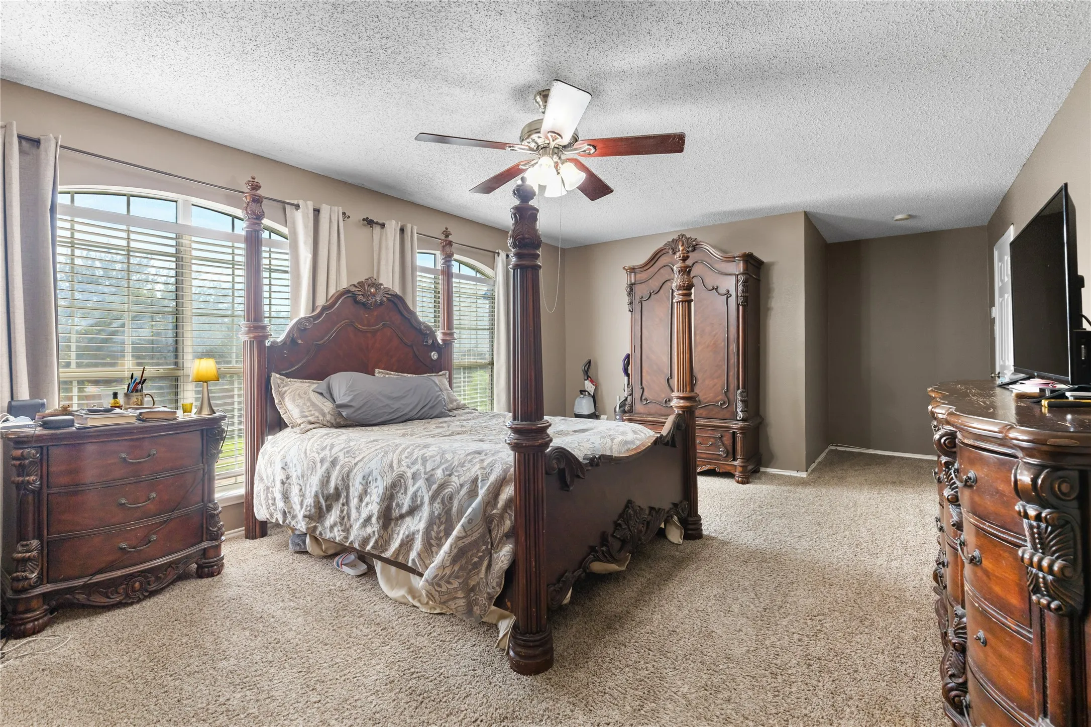 Carpeted room with arched windows, a ceiling fan with light, and neutral wall paint
