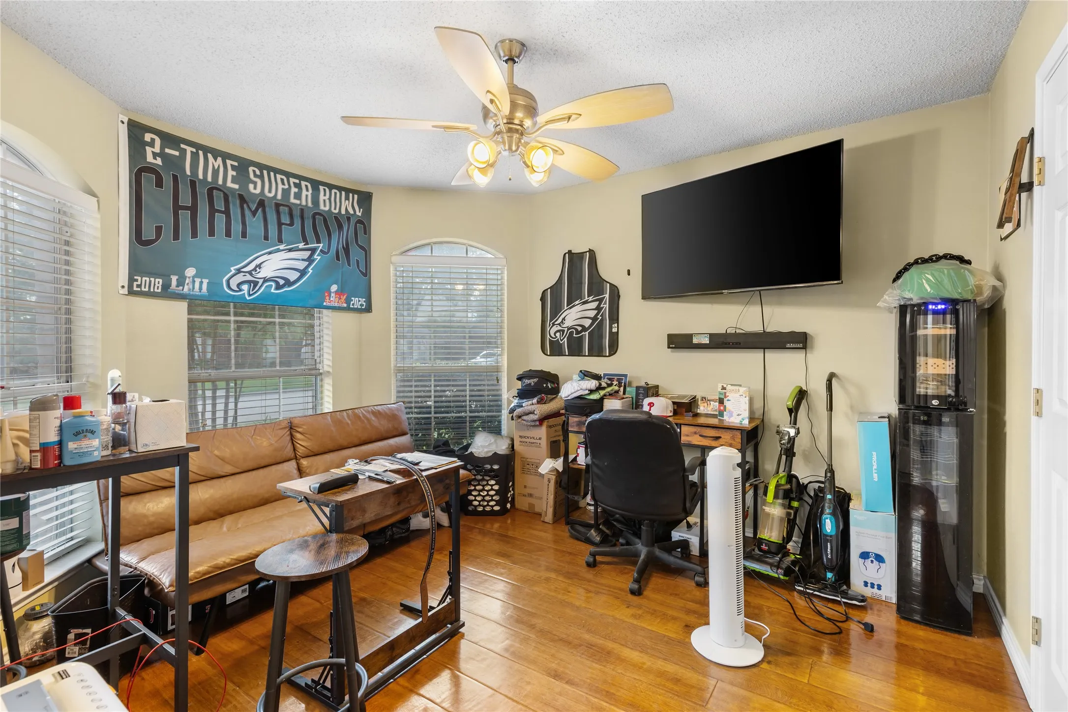 Interior room featuring wood-finish flooring, two arched windows with blinds, and a ceiling fan with integrated lighting