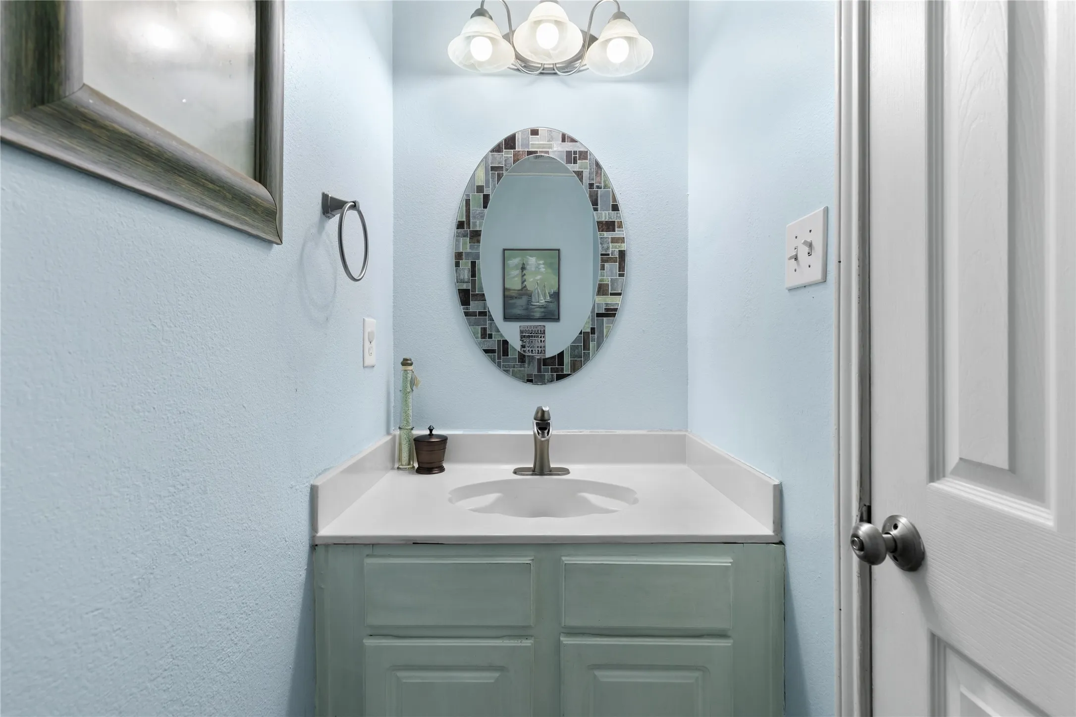 Bathroom vanity featuring an oval mirror with a decorative frame, a single basin sink, a light-toned countertop, and a light green cabinet base