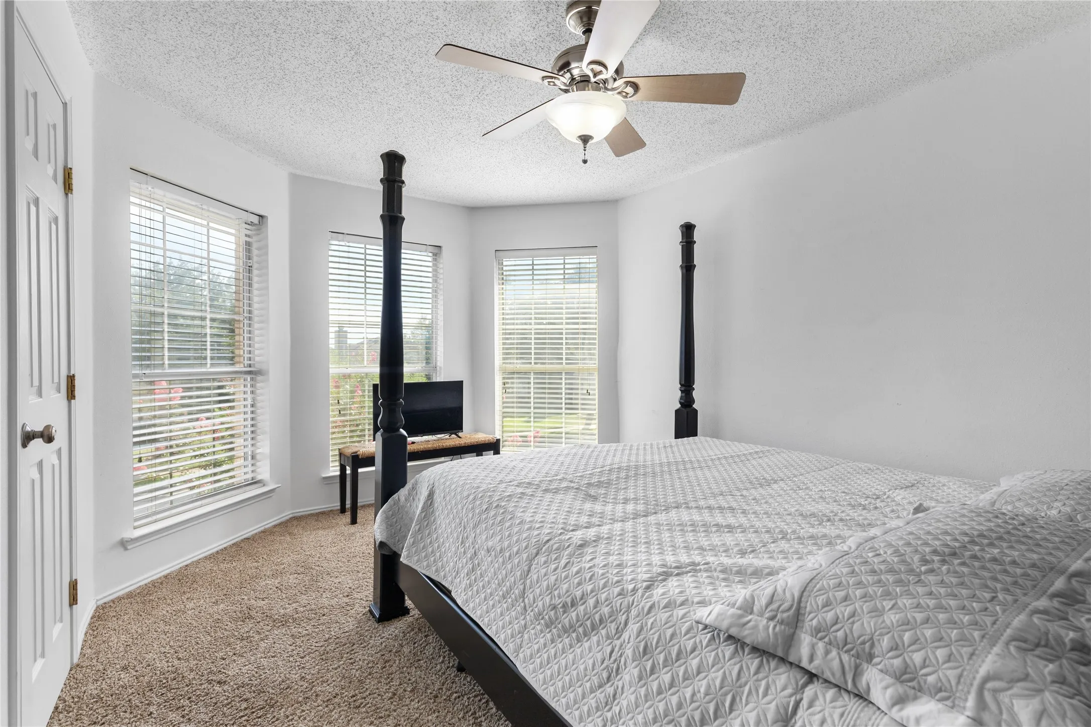 Bedroom featuring a bay window with multiple windows, textured carpet flooring, and a ceiling fan with integrated lighting