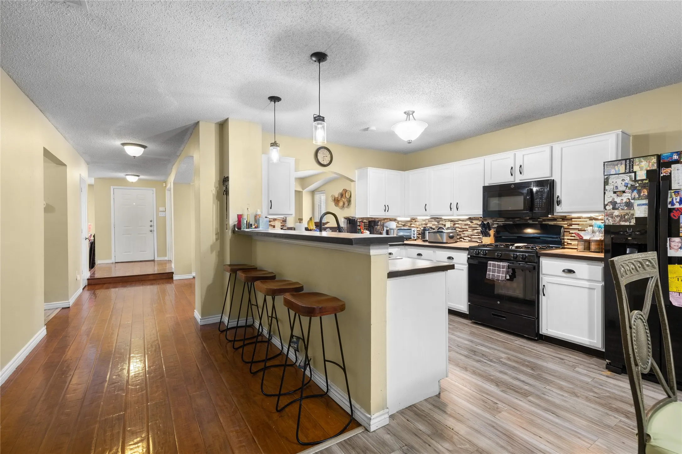 Kitchen featuring white cabinetry, black appliances, a tiled backsplash, and a breakfast bar with pendant lighting