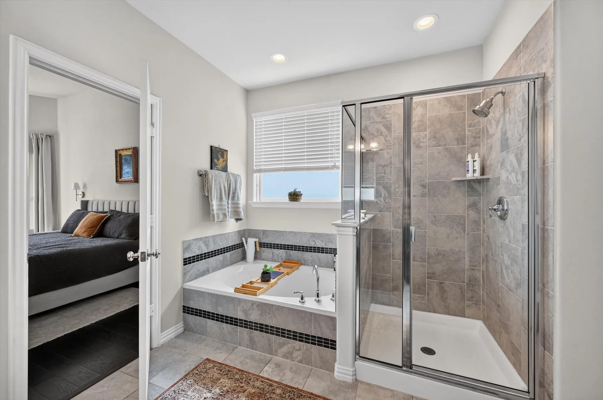 Spacious bathroom featuring a glass-enclosed shower, a large soaking tub with tile surround, a window with horizontal blinds, recessed lighting, and tile flooring