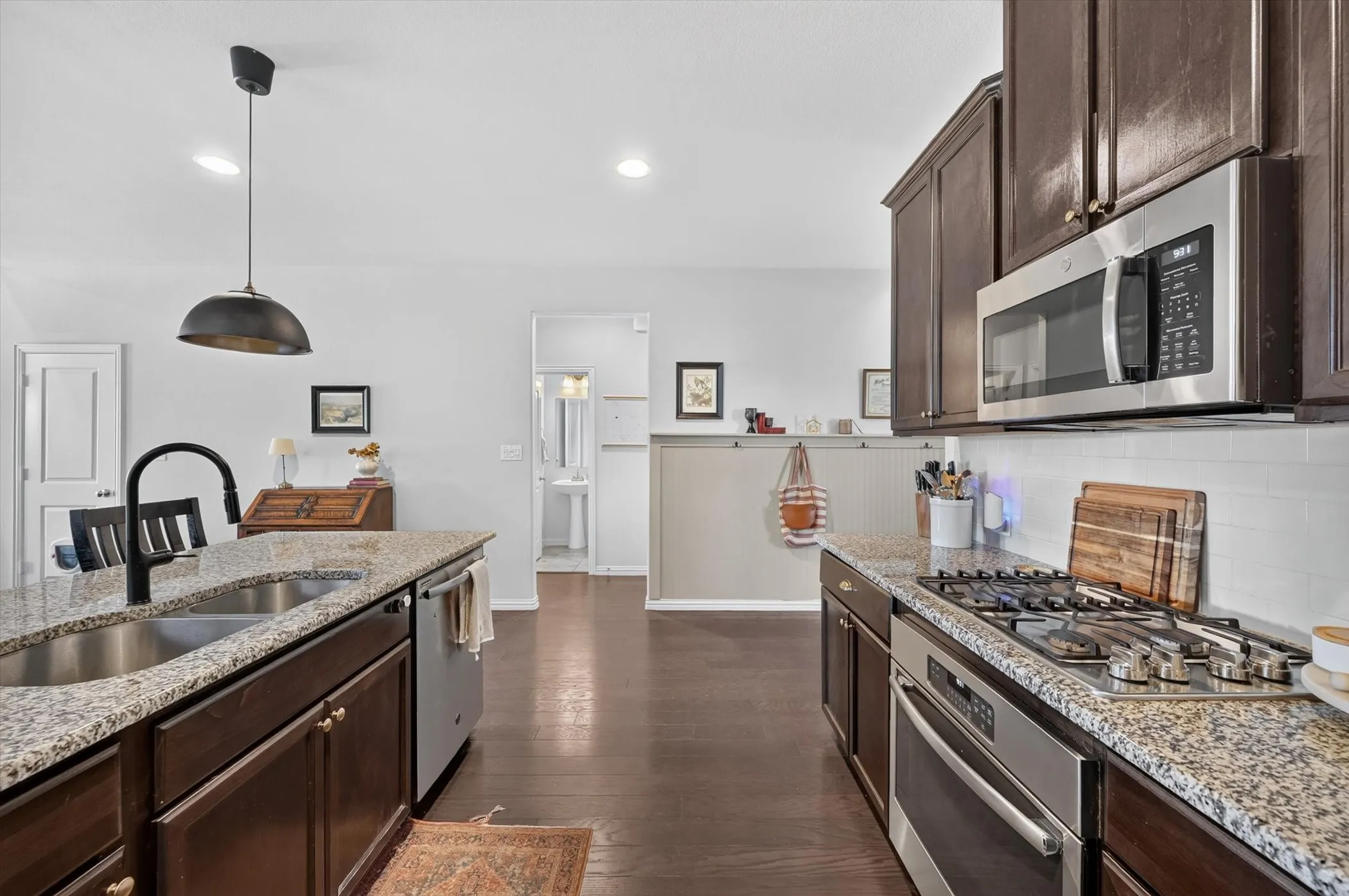 Modern kitchen featuring dark wood-finish cabinetry, speckled granite countertops, and stainless steel appliances including a gas range and microwave
