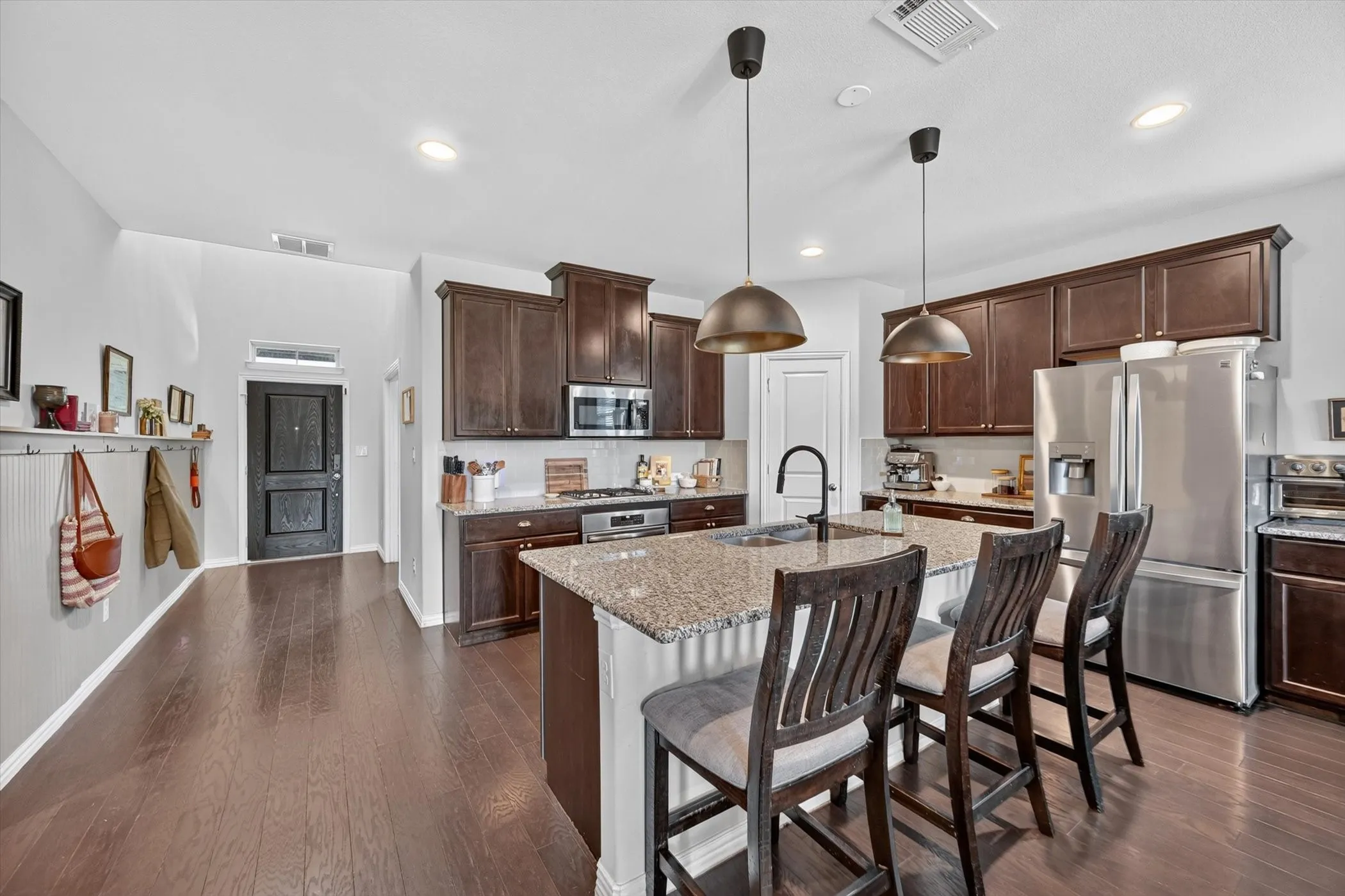 Open-concept kitchen featuring an oversized island with seating, stainless steel appliances, dark wood cabinetry, and granite countertops
