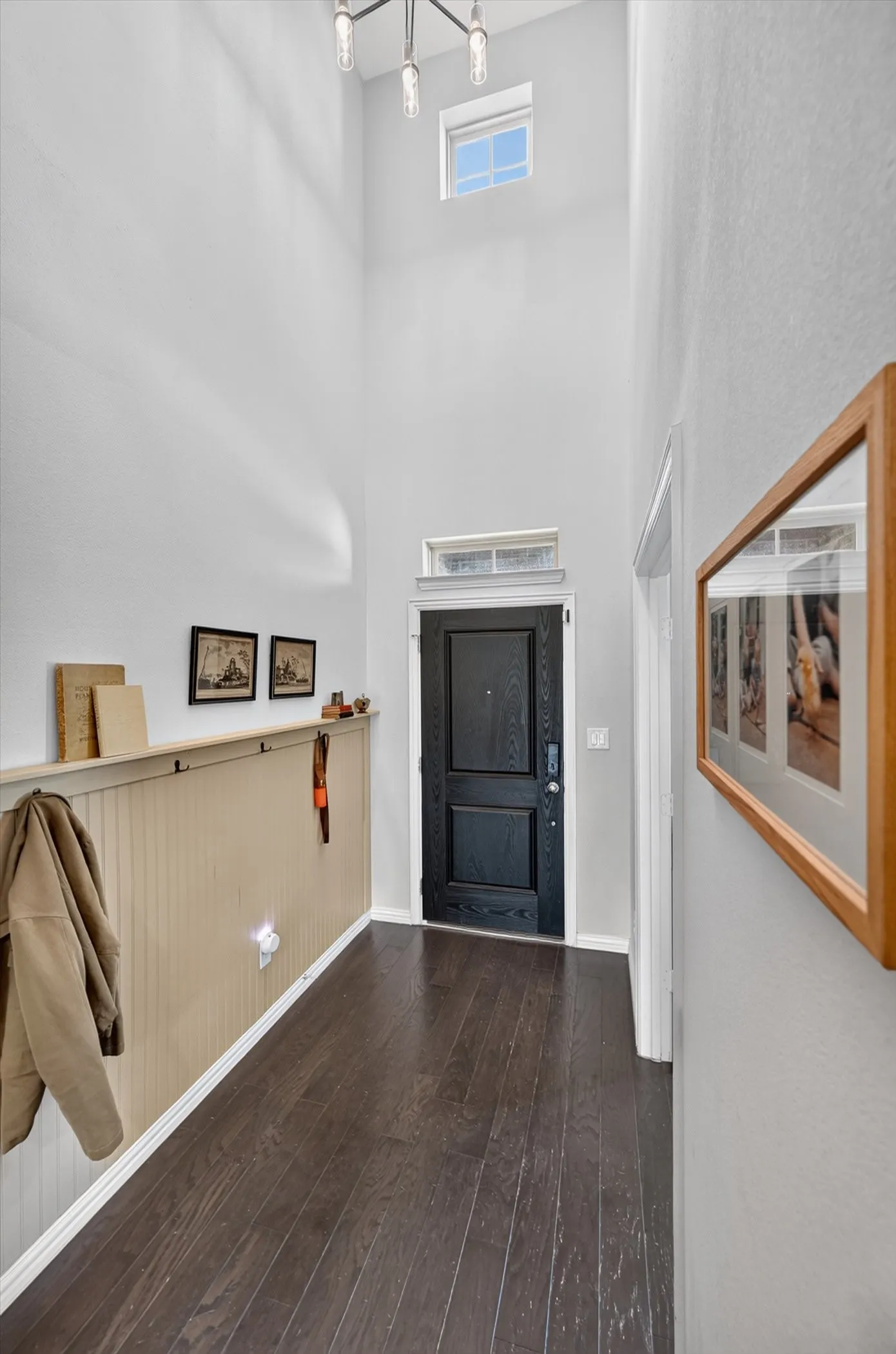 Entryway featuring high ceilings, wood-finish flooring, a dark paneled door with transom window, beadboard wainscoting, and a contemporary light fixture