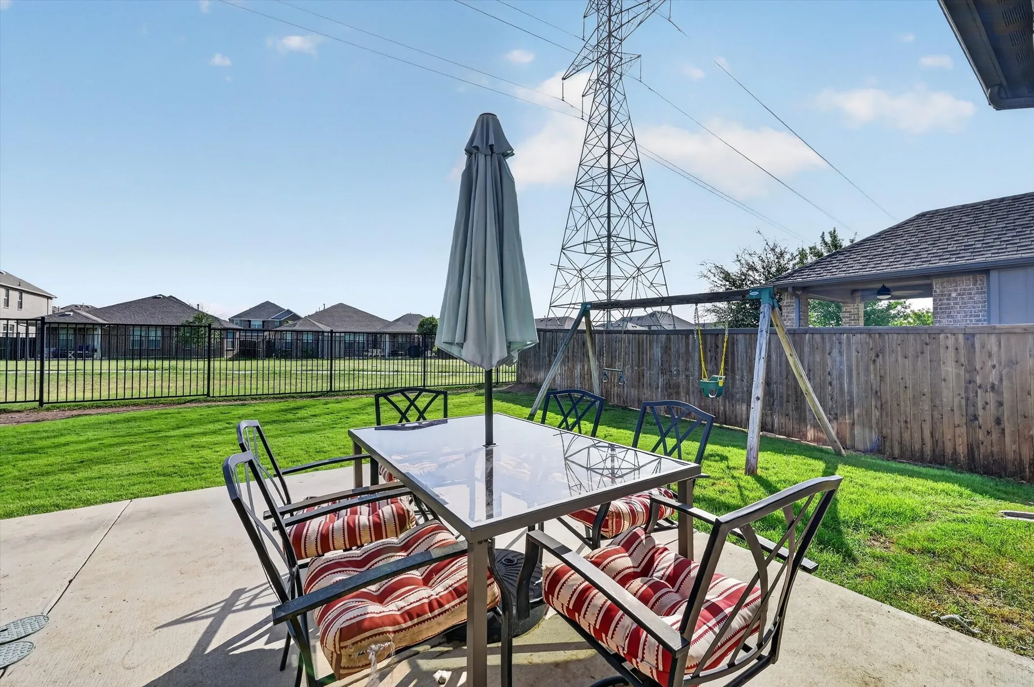 Concrete patio area with a manicured lawn, partial wood privacy fencing, and black wrought iron fencing