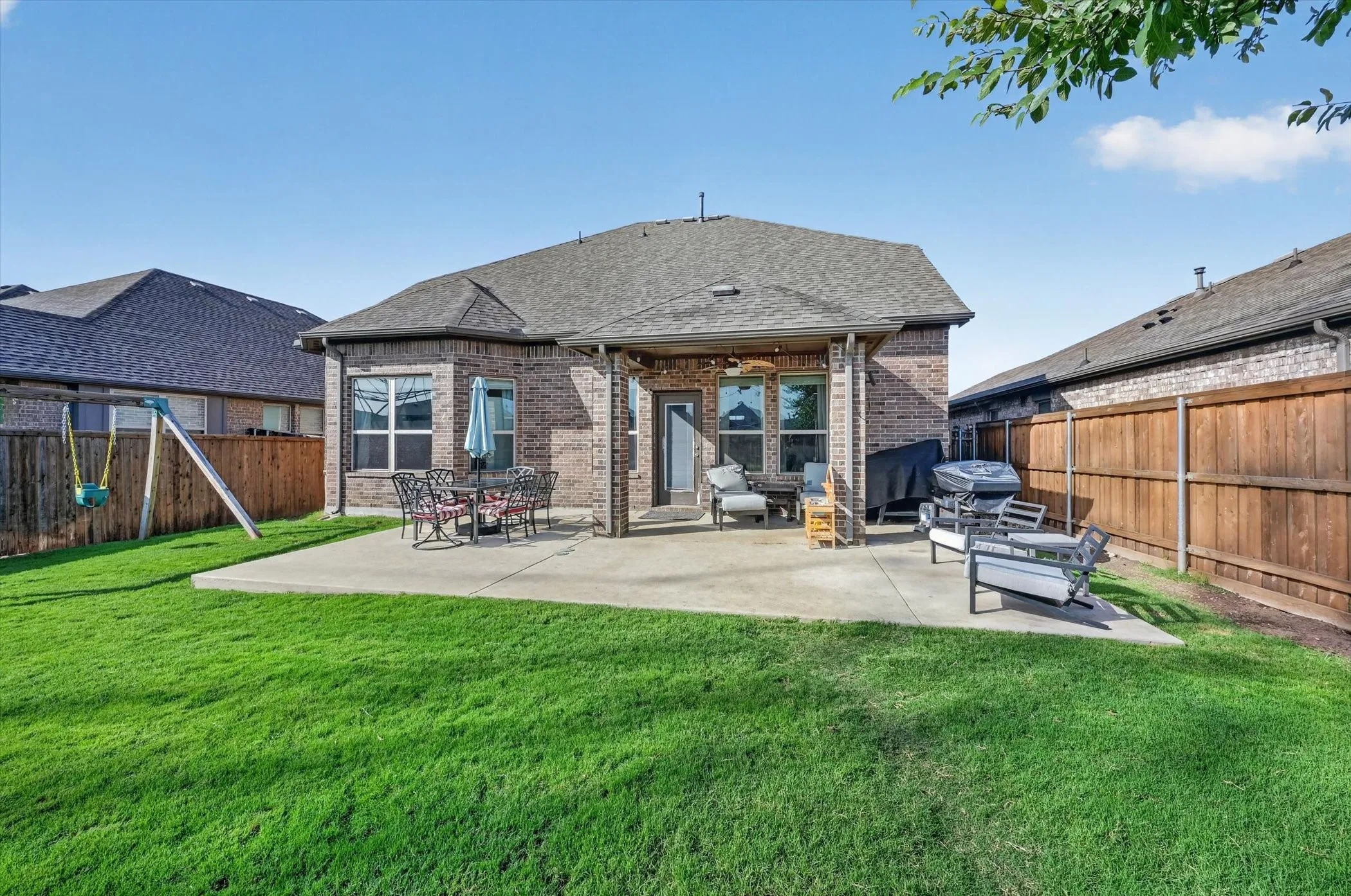 Expansive rear yard featuring a concrete patio, covered outdoor living space, brick exterior, and wood privacy fencing
