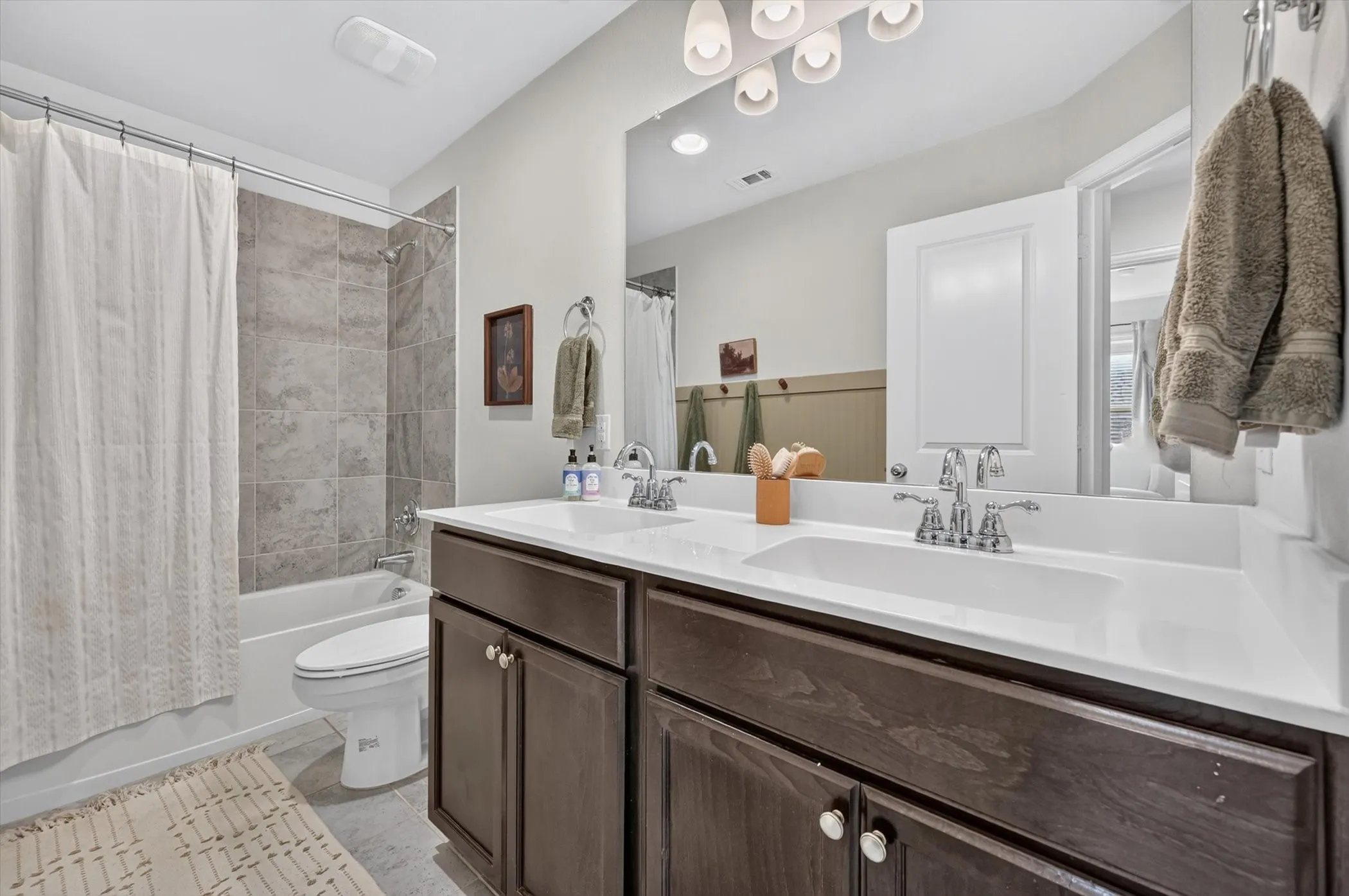 Modern bathroom featuring a double vanity with dark wood-finish cabinetry, white countertops, and chrome fixtures