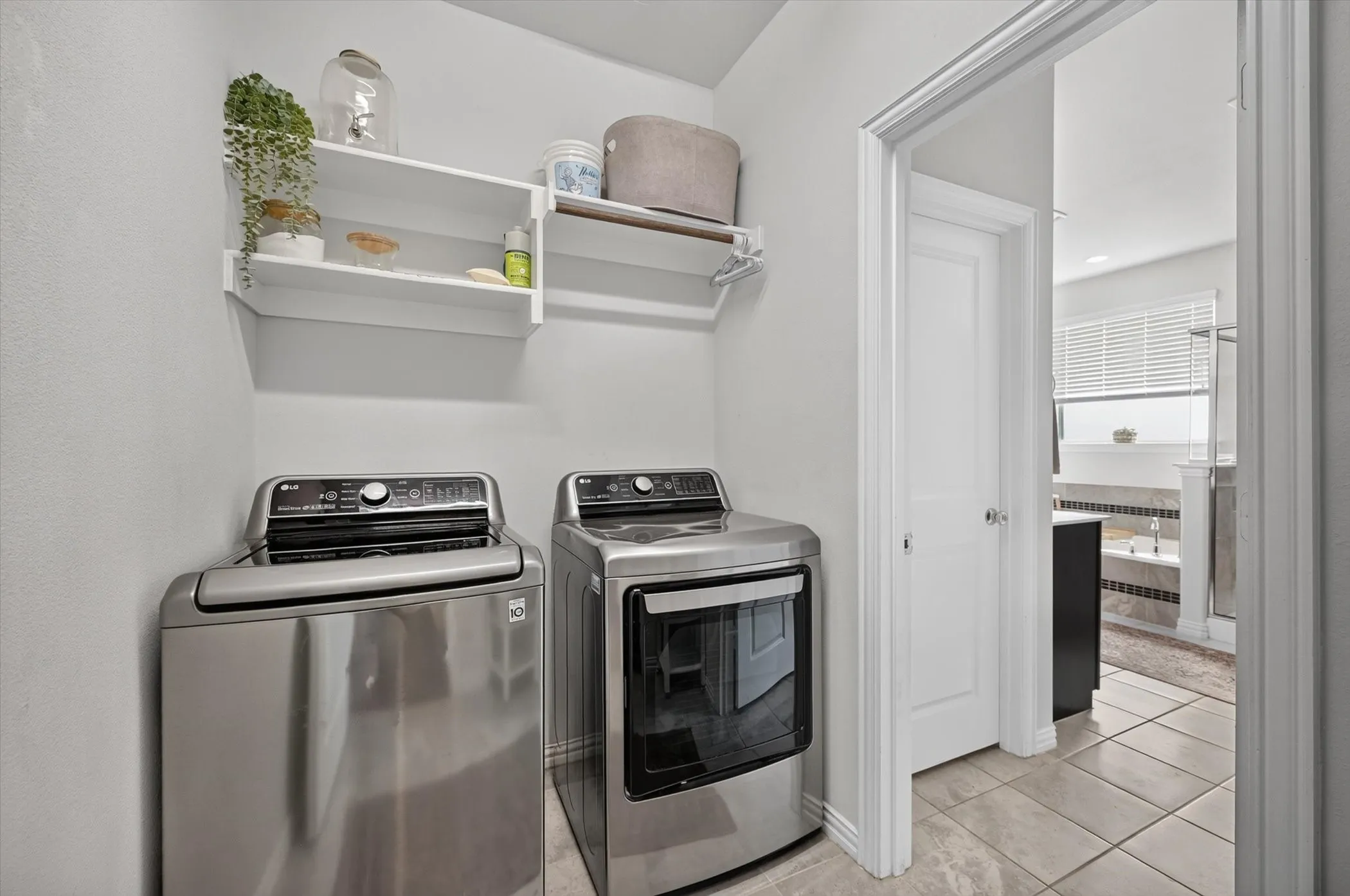 Laundry area featuring wall-mounted shelving, a hanging rod, and tile flooring