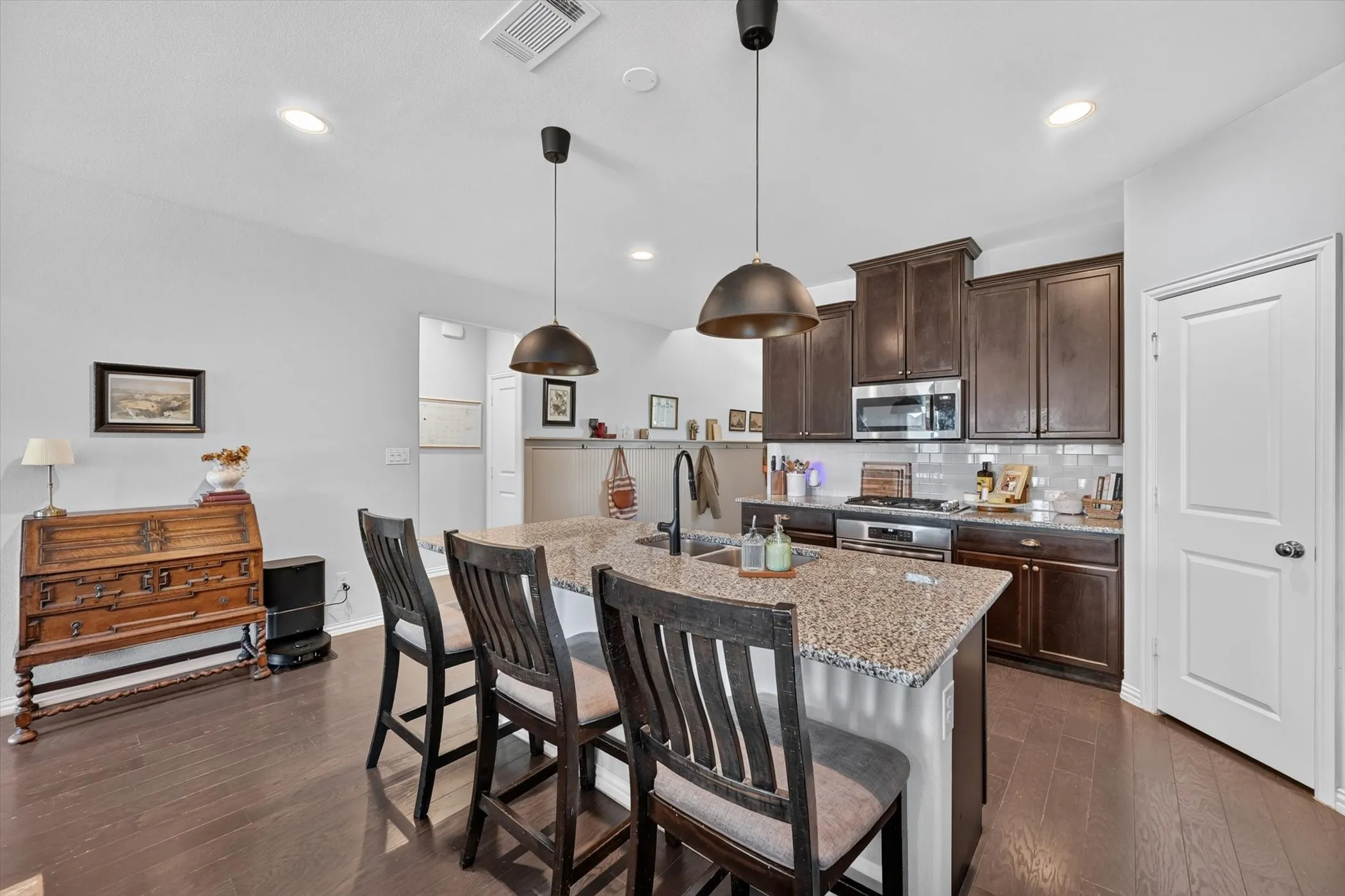 Kitchen featuring a spacious island with a granite-style countertop, dark wood-finish cabinetry, stainless steel appliances, and a subway tile backsplash