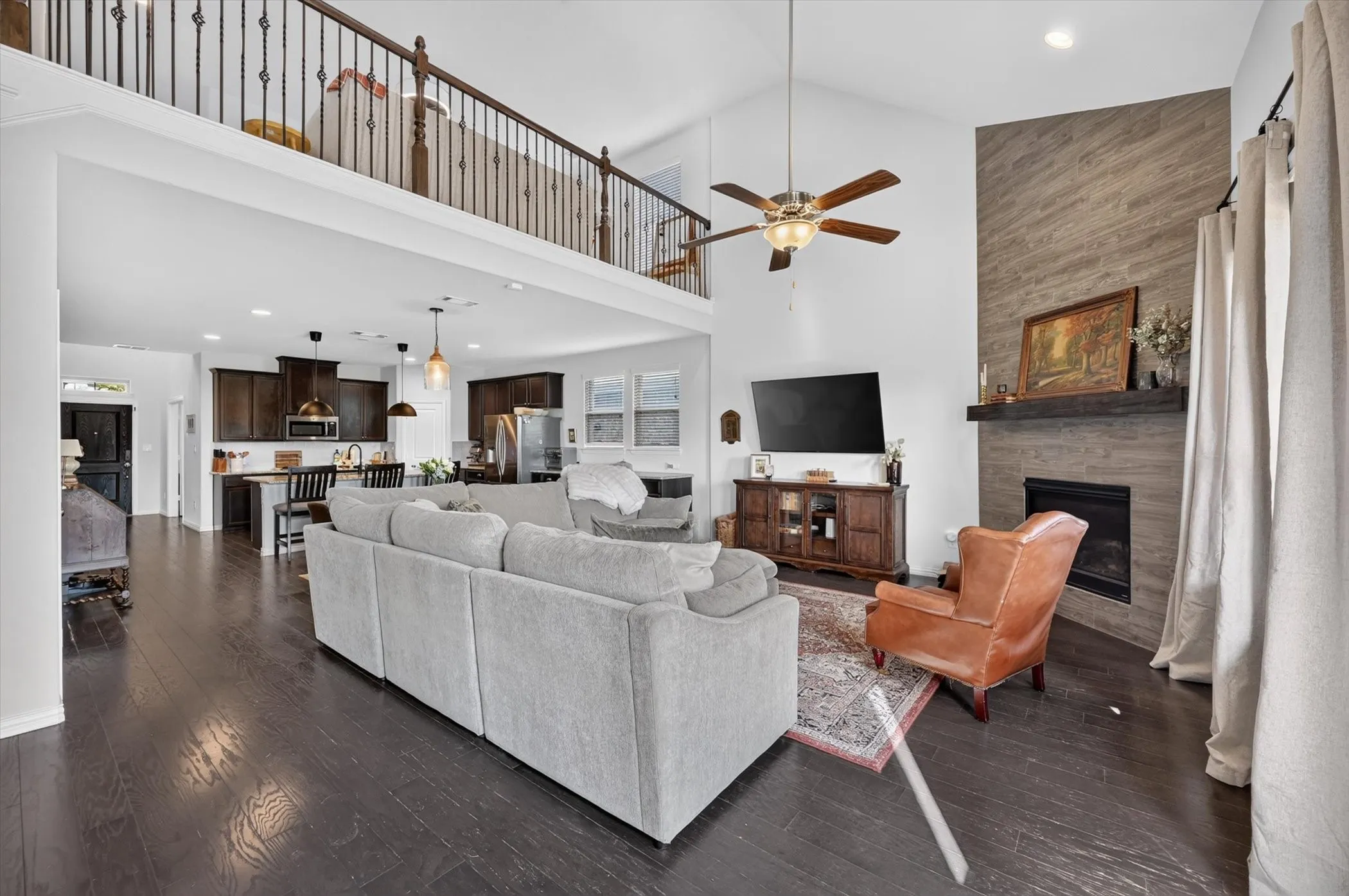 Spacious living area featuring high vaulted ceilings, dark wood-finish flooring, and a fireplace with a stone-clad surround and wood mantel