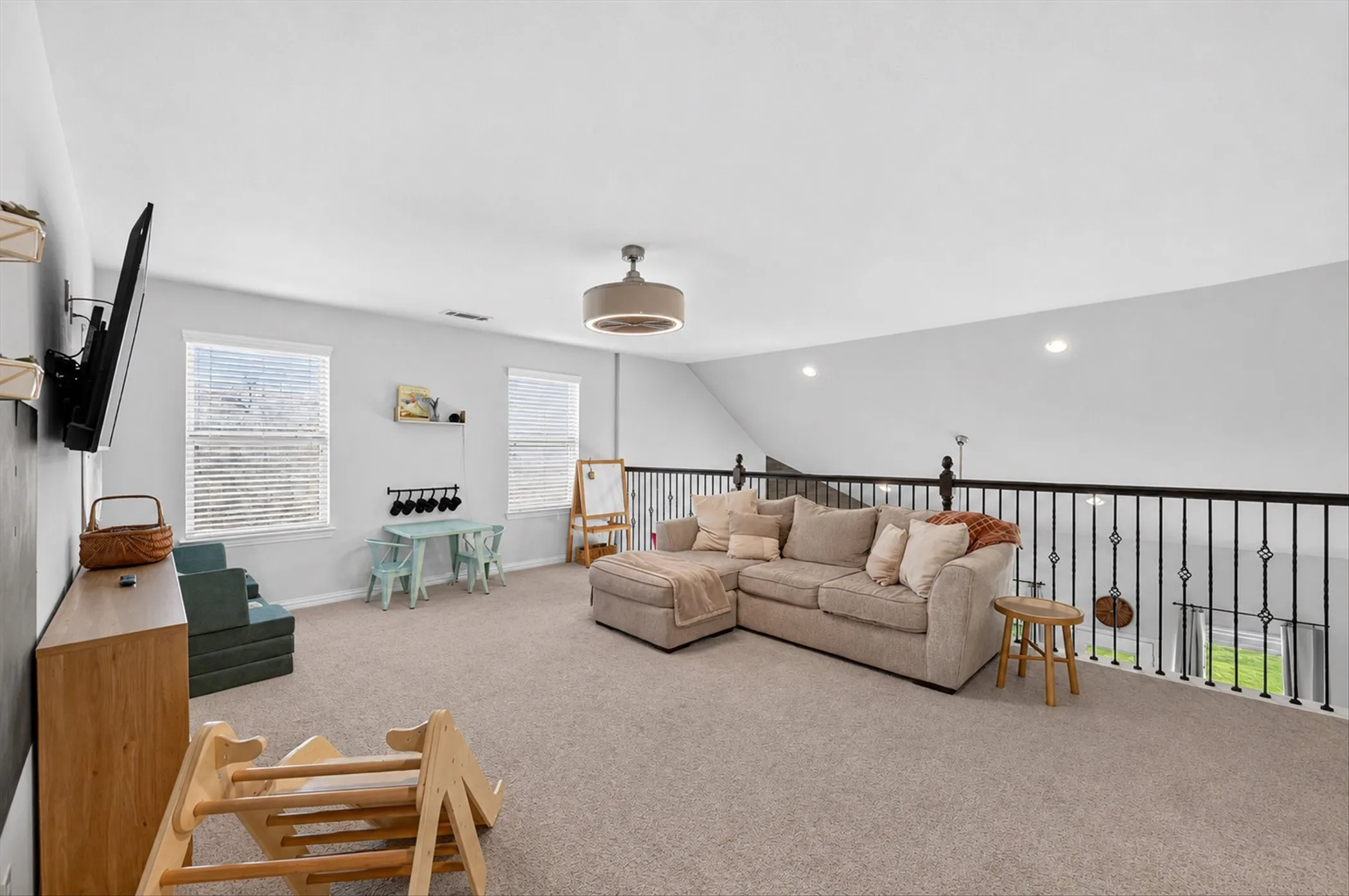Carpeted loft space featuring an open railing, two windows with blinds, a ceiling fan, and recessed lighting