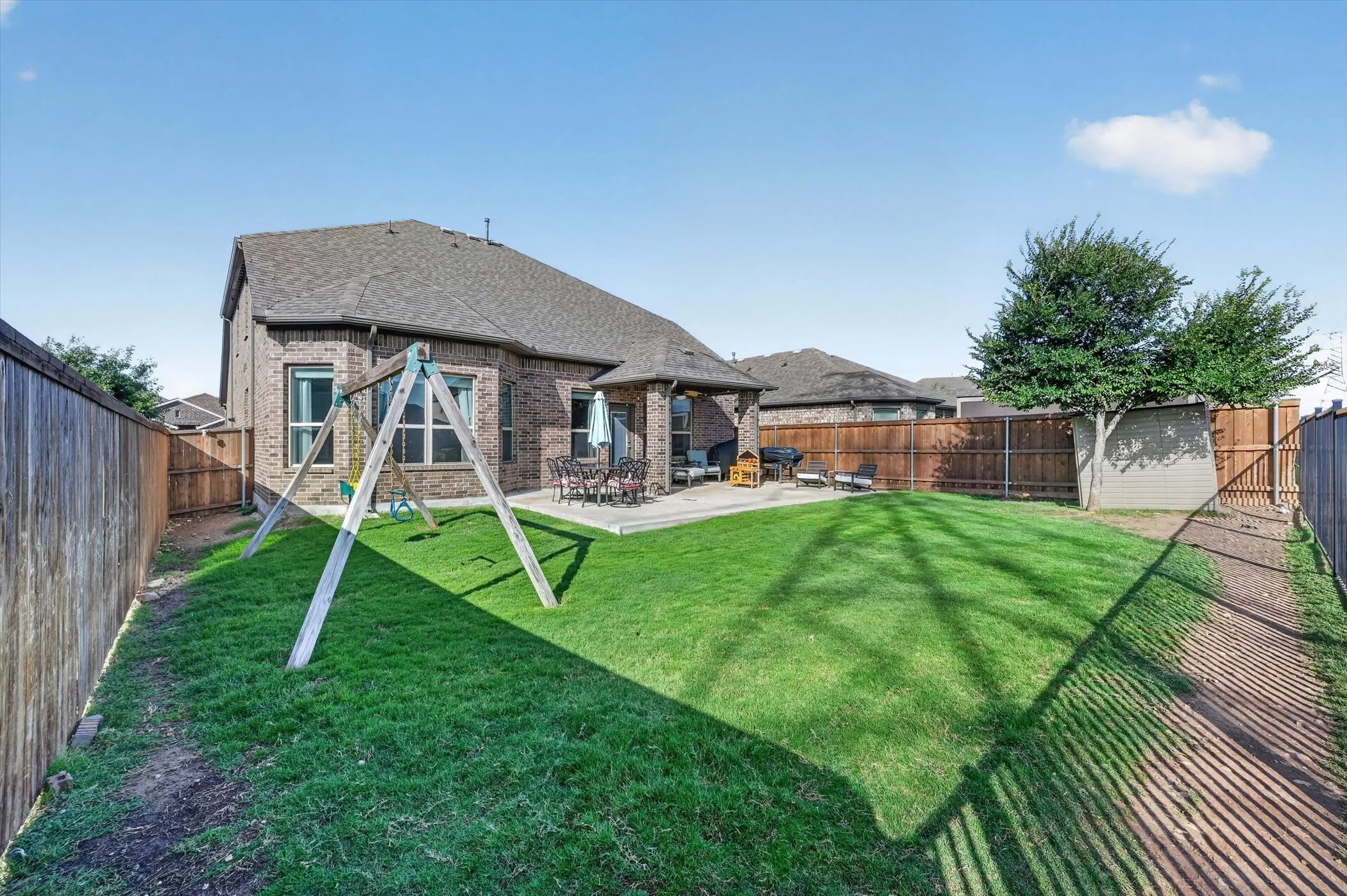 Expansive backyard featuring a manicured lawn, brick exterior, concrete patio, and a privacy fence