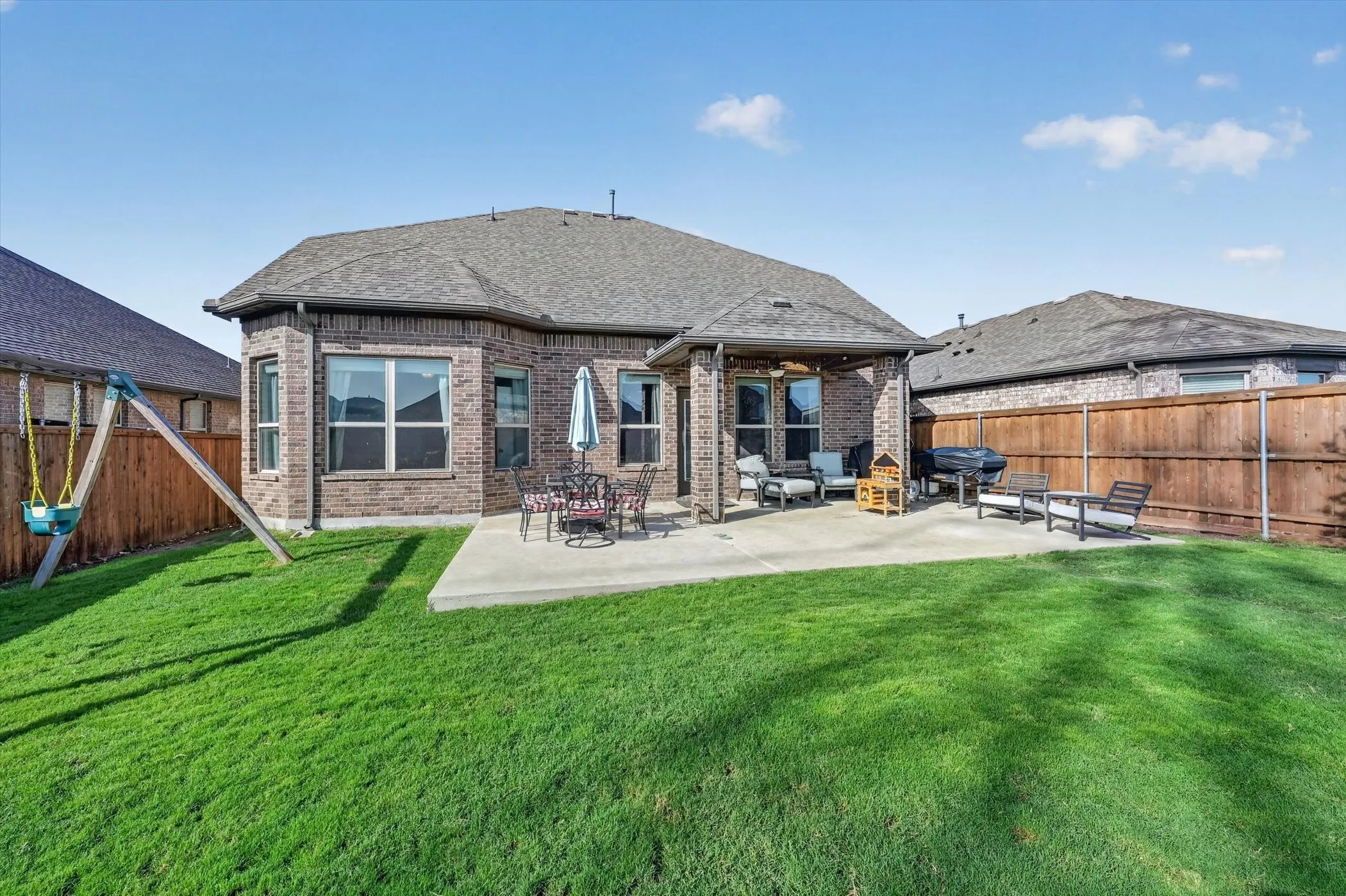 Expansive fenced backyard featuring a substantial concrete patio, a covered outdoor living area, brick exterior, and a well-maintained lawn
