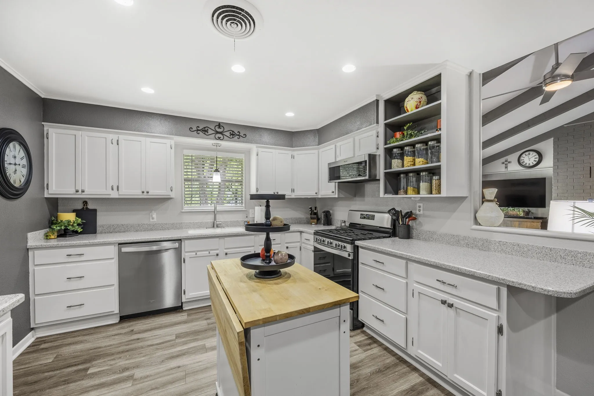 Kitchen featuring white cabinetry, wood-finish flooring, recessed lighting, stainless steel appliances, and a pass-through window with a bar-height corian counter tops
