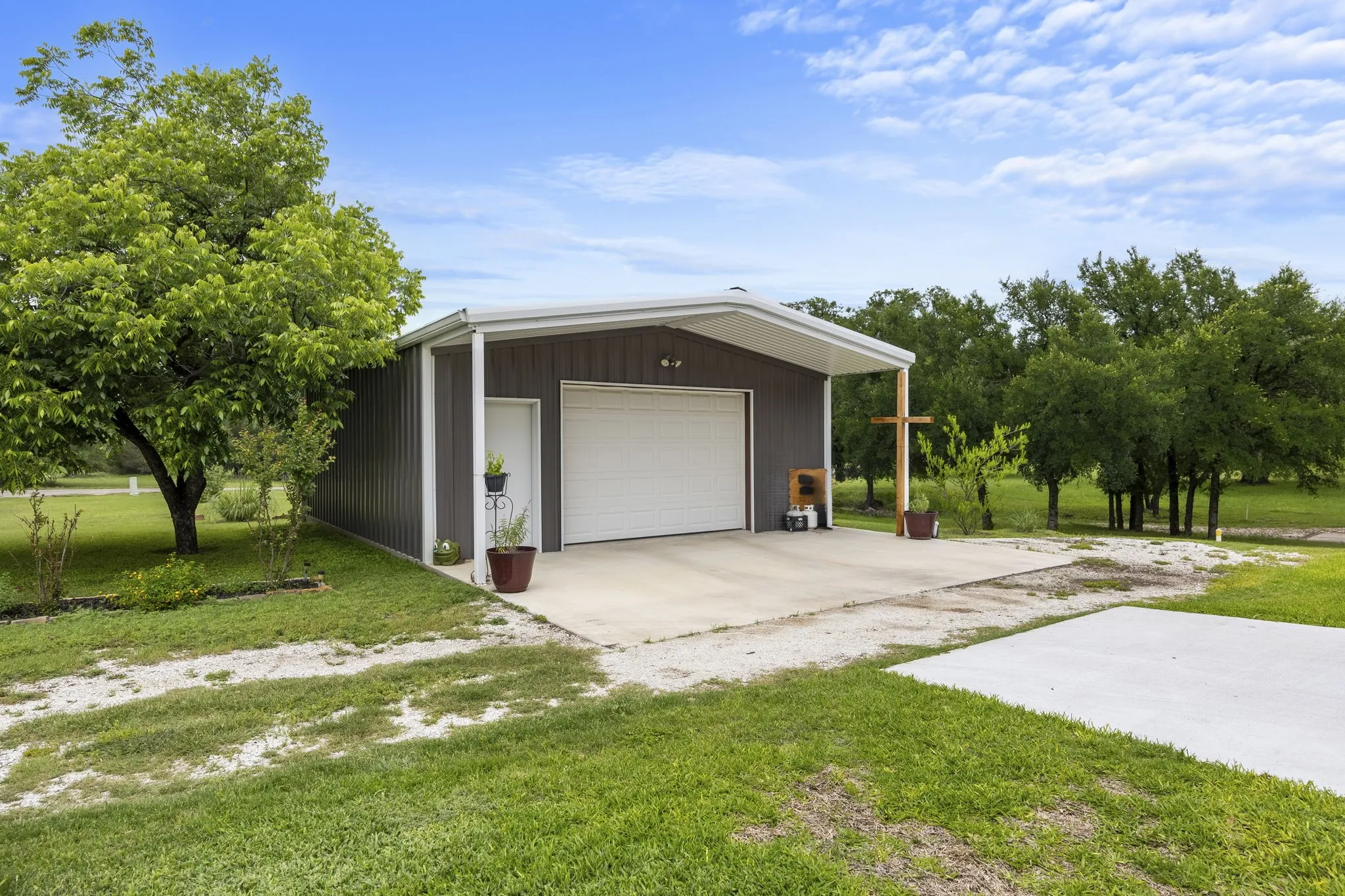 Detached metal building featuring a two-car garage with an overhead door, an exterior pedestrian door, and an extended covered concrete pad