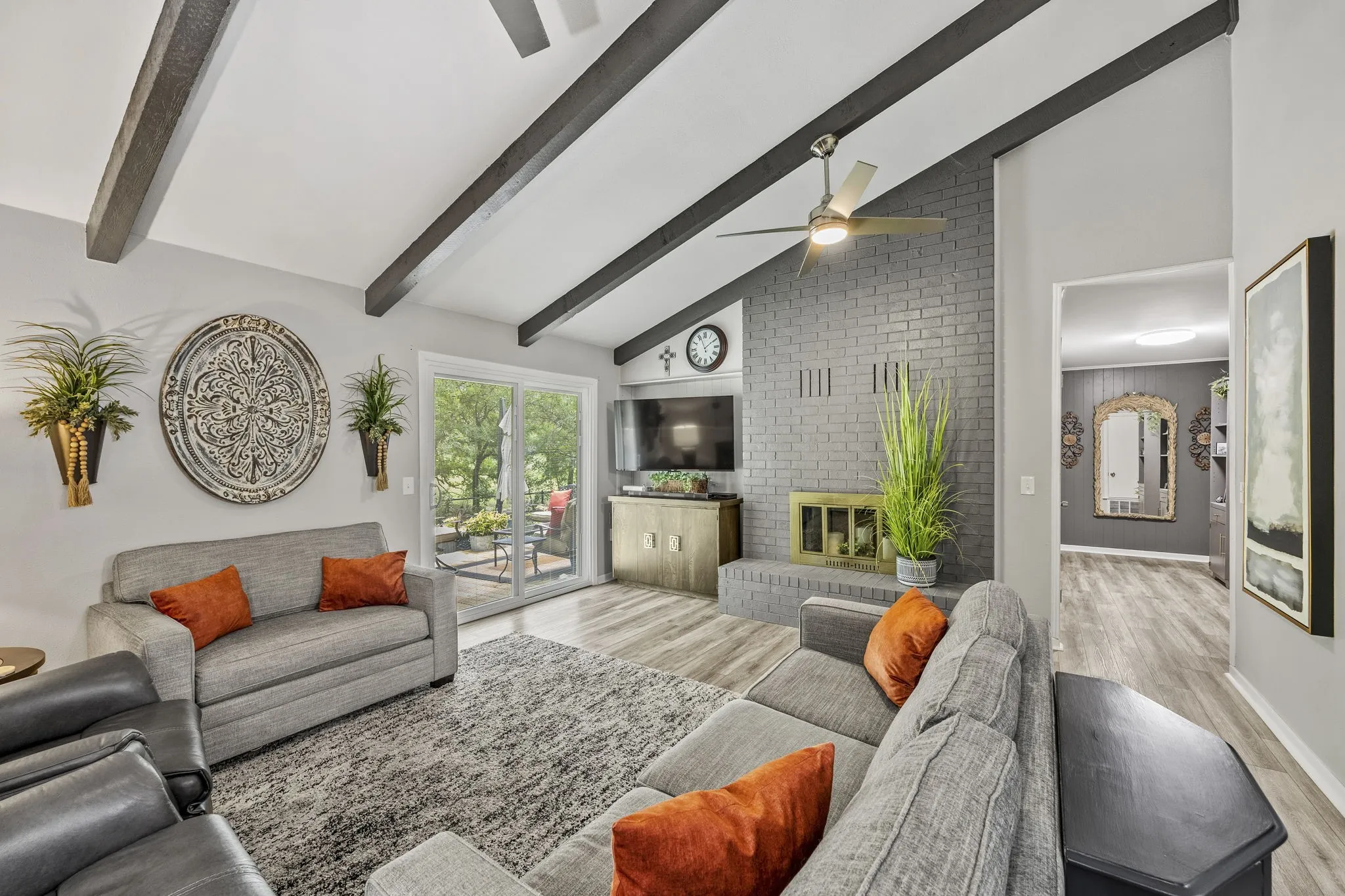 Living room featuring vaulted ceilings with exposed beams, a painted brick fireplace, wood-finish flooring, and sliding glass doors opening to an outdoor patio