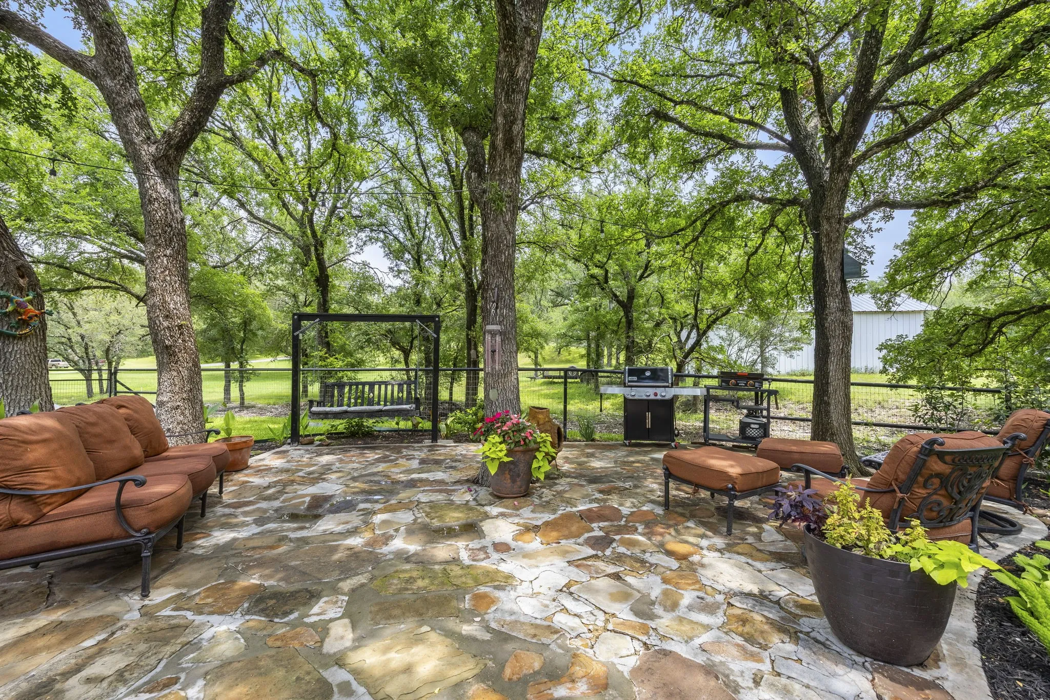 Stone patio featuring mature trees, a metal swing, and a built-in outdoor grilling area