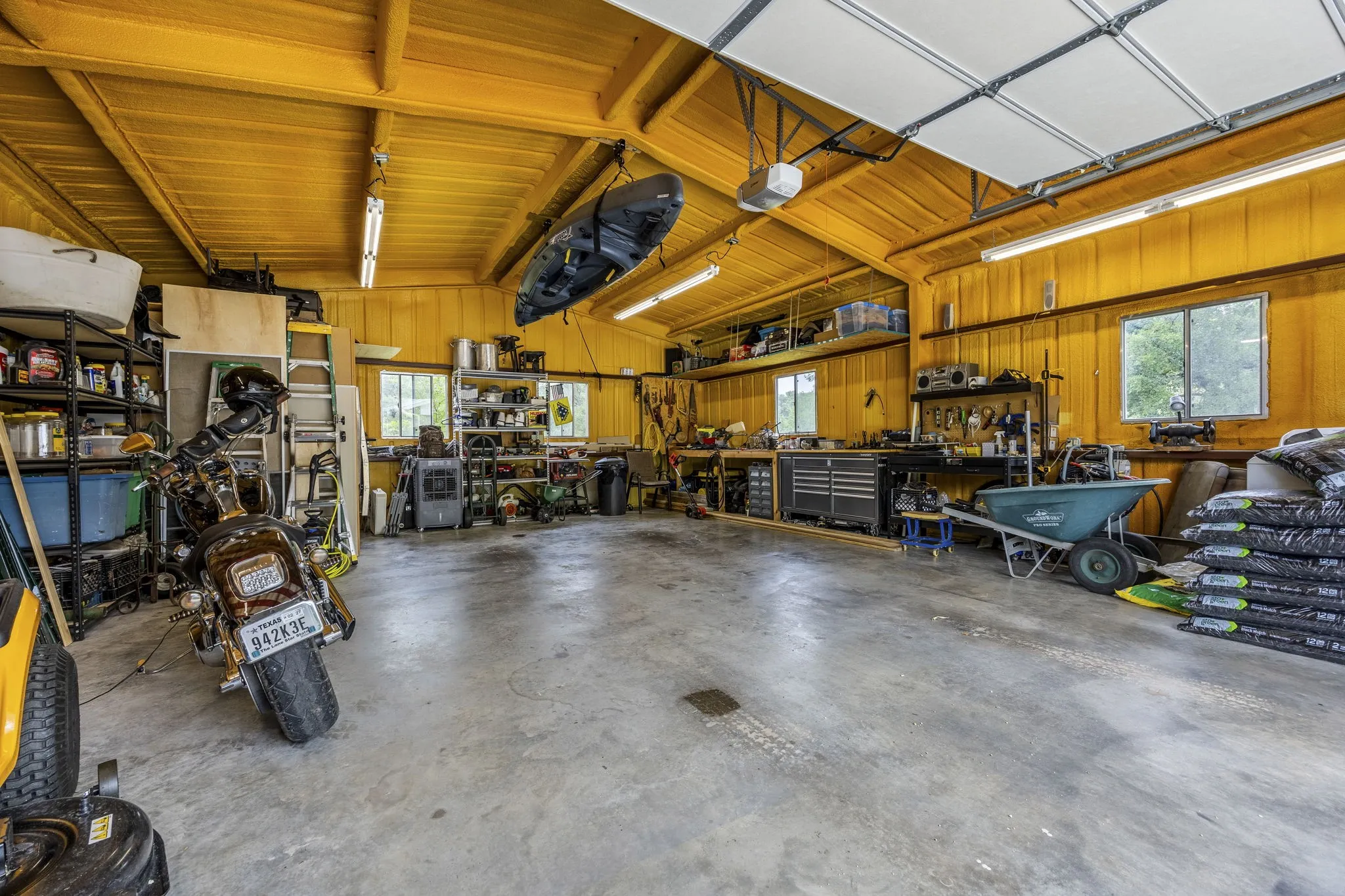 Spacious garage featuring a high vaulted ceiling, concrete flooring, multiple windows, and extensive built-in shelving
