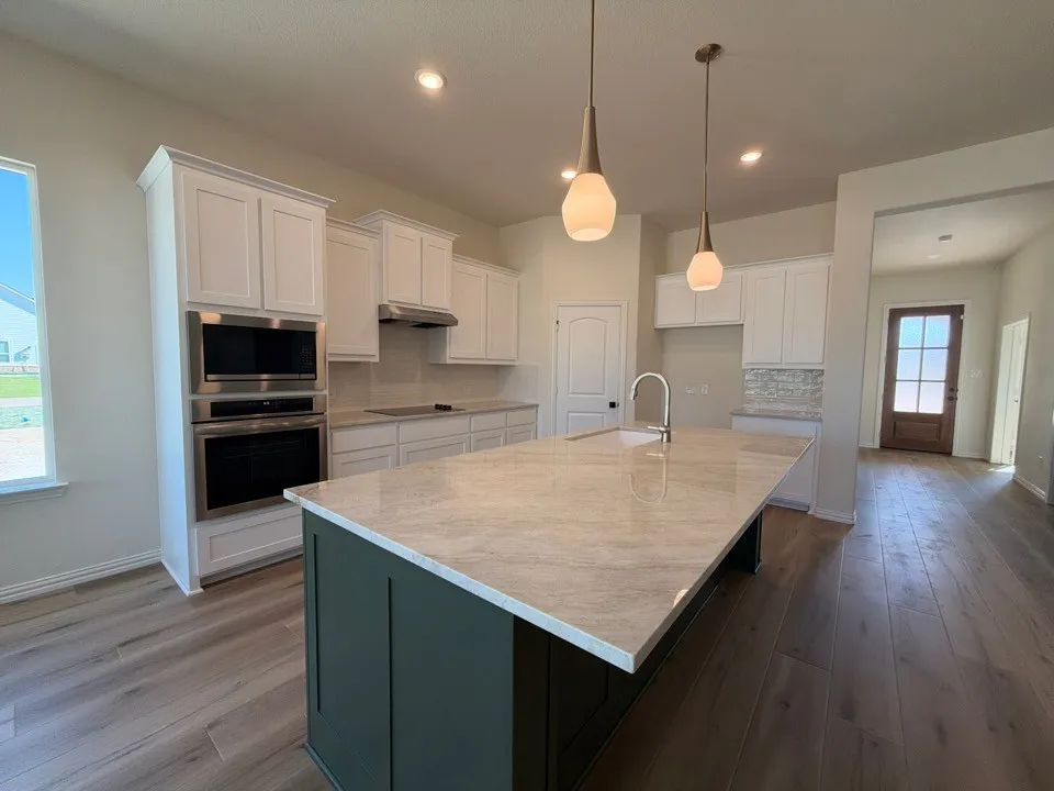 Kitchen with wood-finish flooring, white cabinetry, integrated stainless steel appliances, and a central island featuring a light-toned countertop and pendant lighting