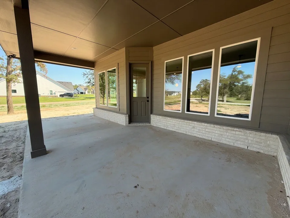 Covered outdoor patio with a concrete surface, featuring a brick-clad exterior wall and multiple large windows