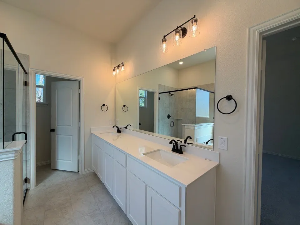 Dual vanity with white cabinetry and integrated sinks, quartz countertops, black fixtures, and framed glass shower enclosure