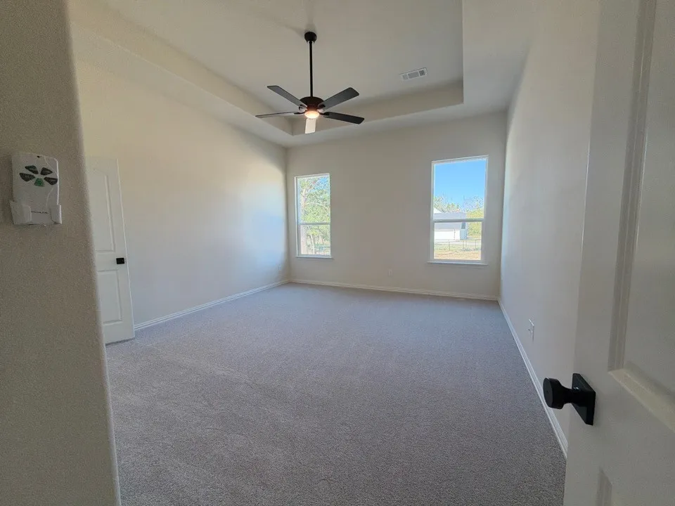 Tray ceiling with recessed lighting, ceiling fan with integrated light, two windows, carpeted flooring, and a white paneled door with a black knob