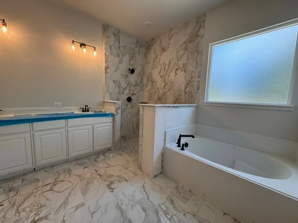 Spacious bathroom featuring a built-in soaking tub, a separate walk-in shower with tiled walls, and a dual vanity with white cabinetry