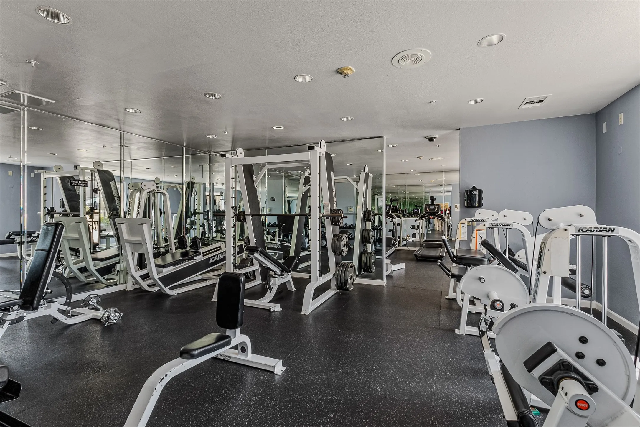 Fitness center featuring extensive mirrored walls, recessed lighting, rubber flooring, and a comprehensive selection of workout equipment