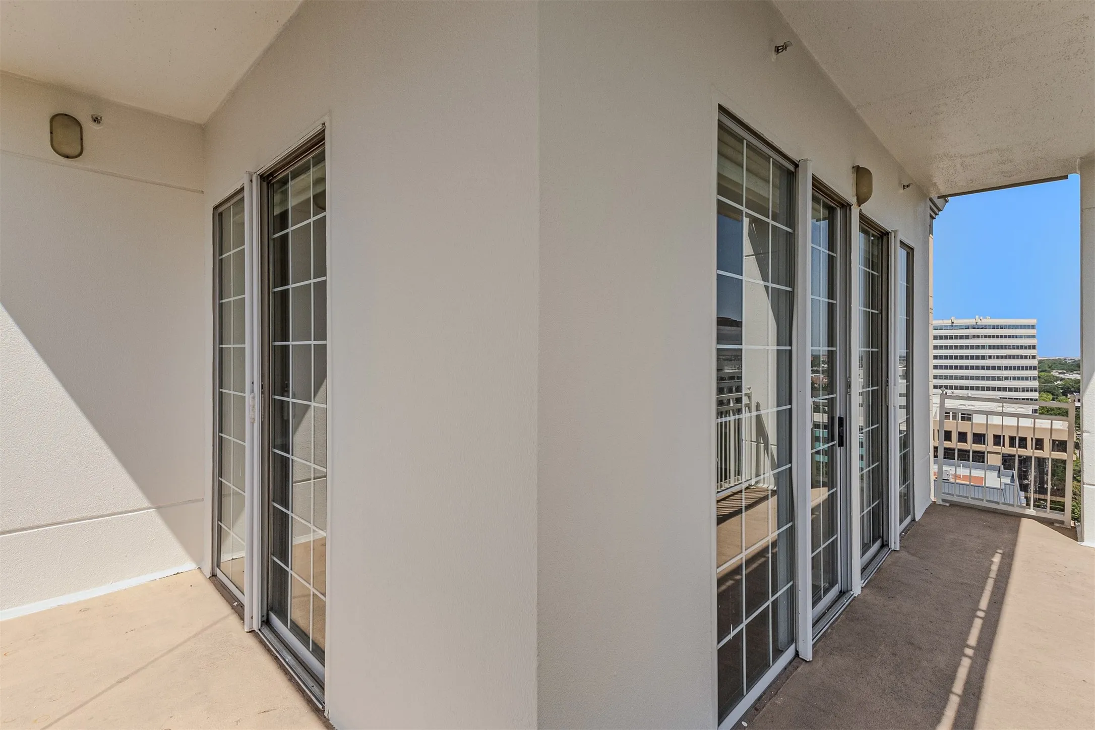 Outdoor patio featuring multiple sliding glass doors with grid patterns, a concrete surface, and white perimeter walls