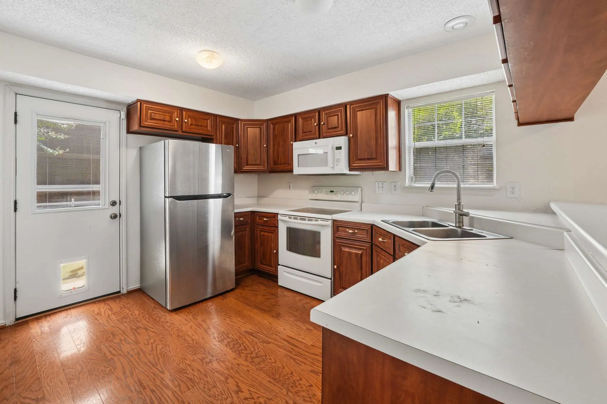 Kitchen featuring wood-finish flooring, rich wood cabinetry, stainless steel refrigerator, white electric range with overhead microwave, and a double basin sink