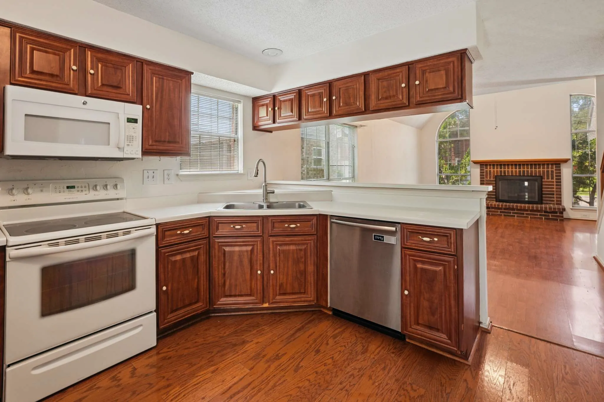 Kitchen featuring wood-finish flooring, white countertops, dark wood cabinetry, white appliances, and a stainless steel dishwasher