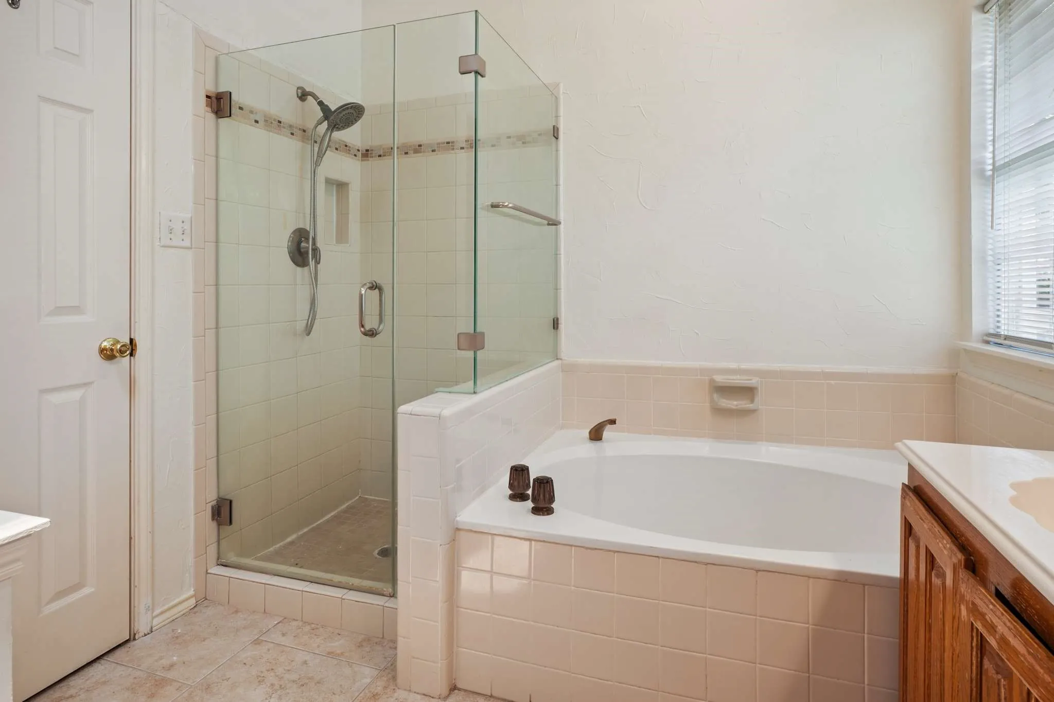 Bathroom featuring a glass-enclosed shower, built-in bathtub, and a window with blinds