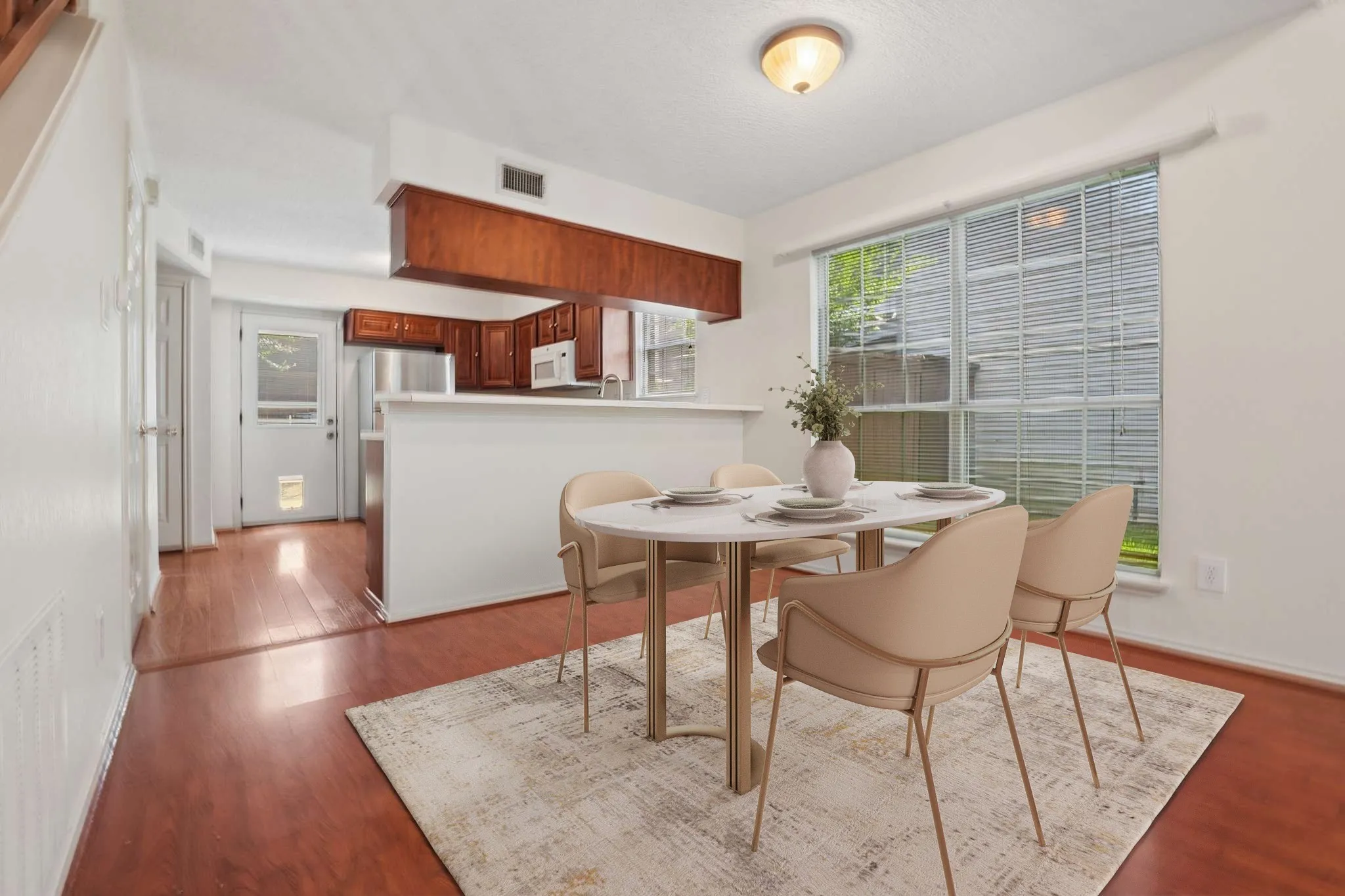 Open-concept dining area with wood-finish flooring, a large window with blinds, and white walls
